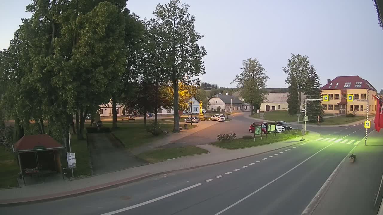 A town square with a few cars, a statue, and several buildings is visible at dusk, under a clear sky.
