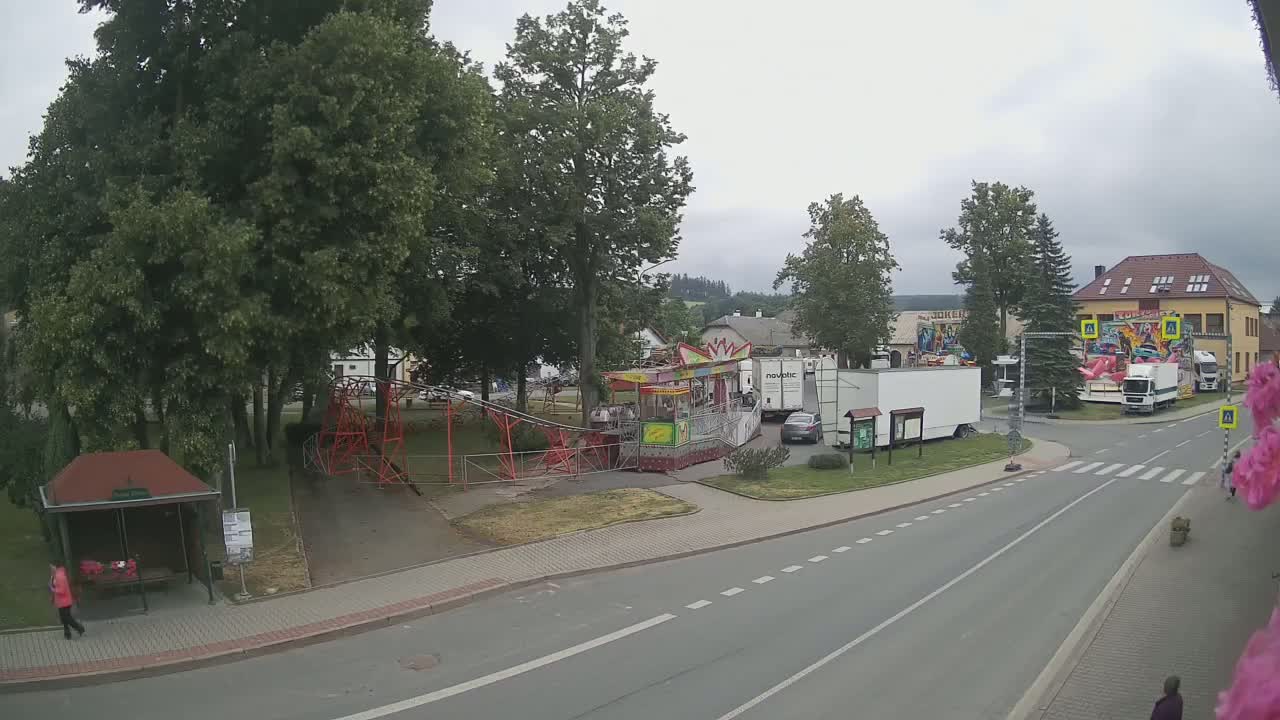 A fairground with several rides and trailers sits beside a paved road on an overcast day in a town with trees and buildings in the background.