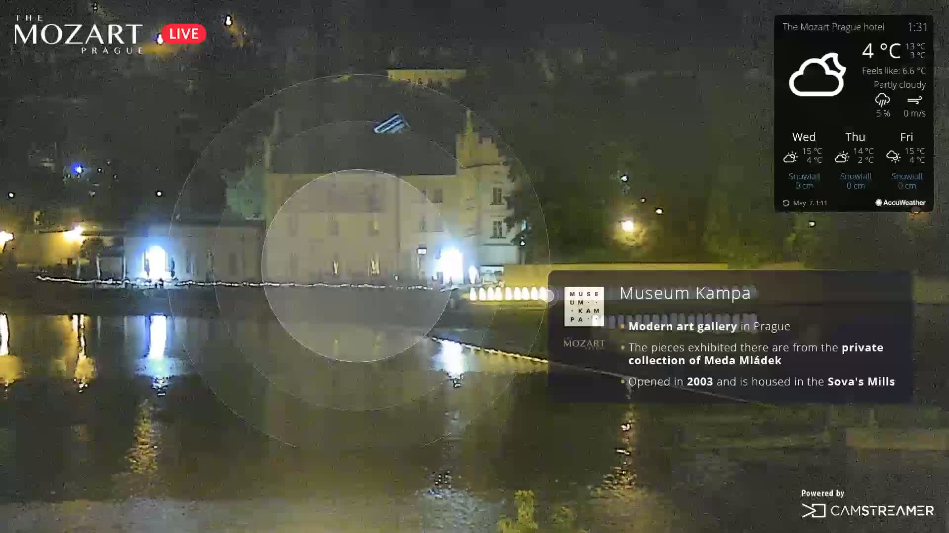 A nighttime, partly cloudy view of a building across a body of water, reflecting lights.