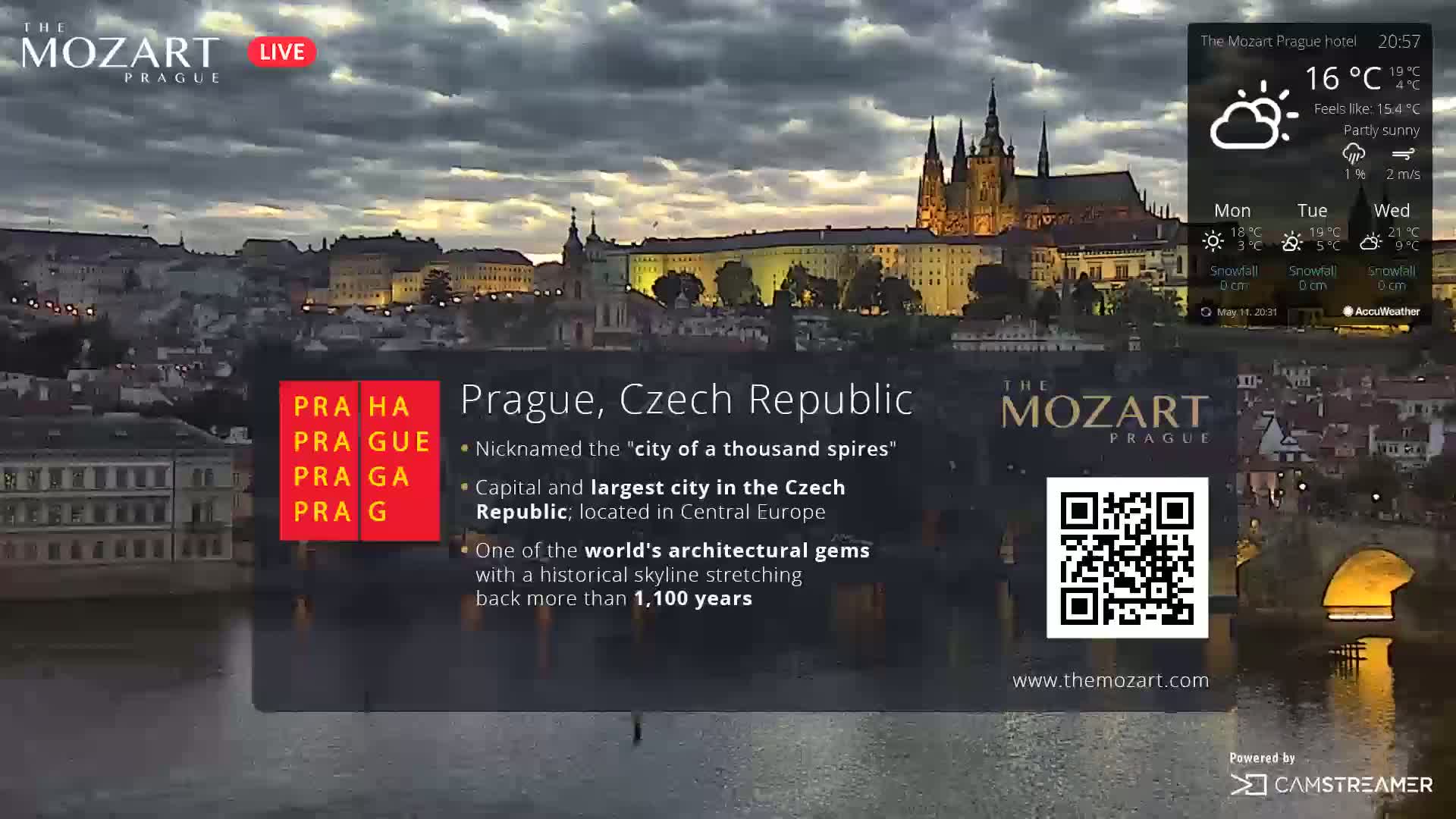 A partly sunny evening view of Prague's illuminated cityscape, overlooking a river.