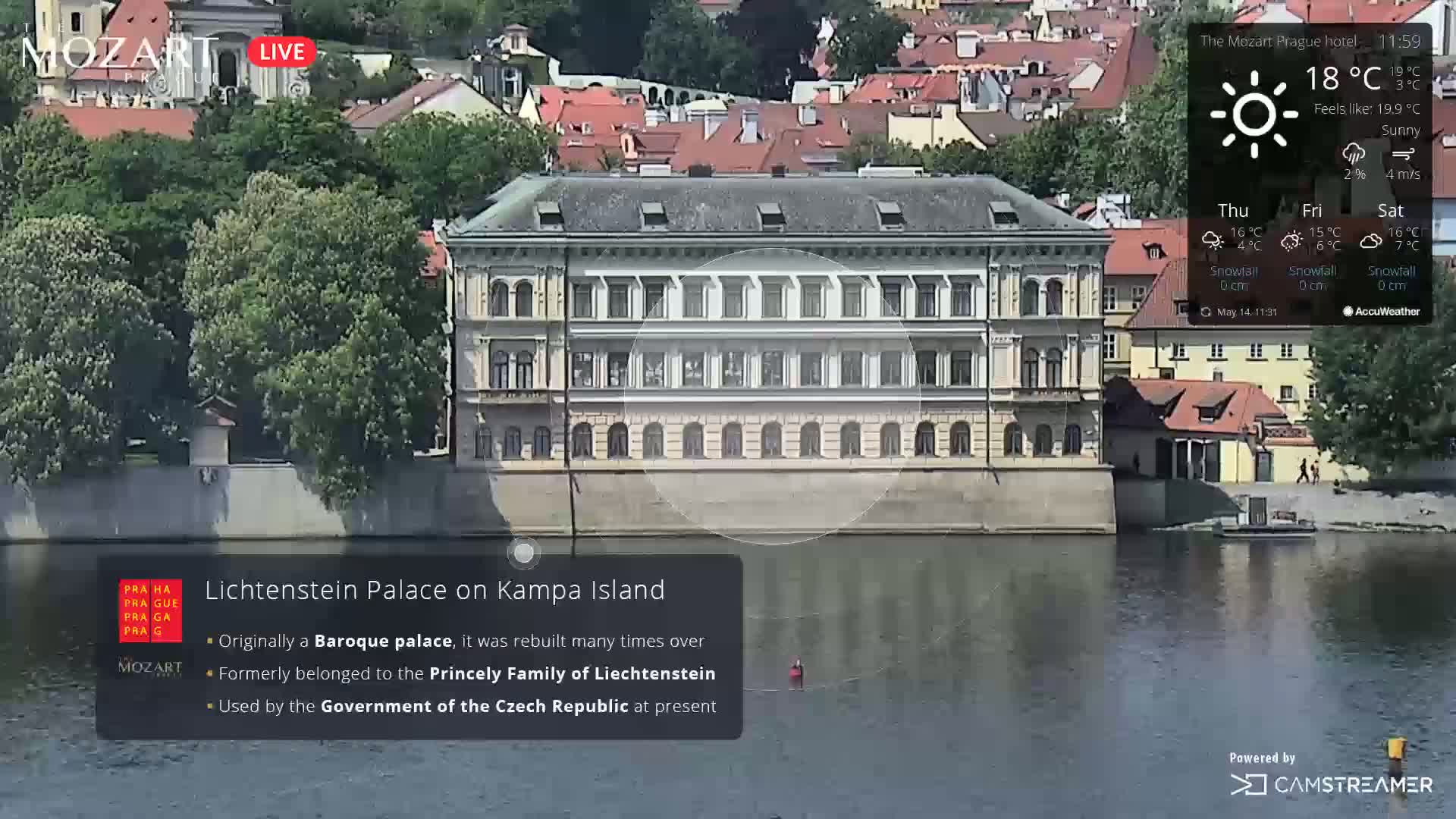 A large, light-colored palace sits on the bank of a river under sunny skies.