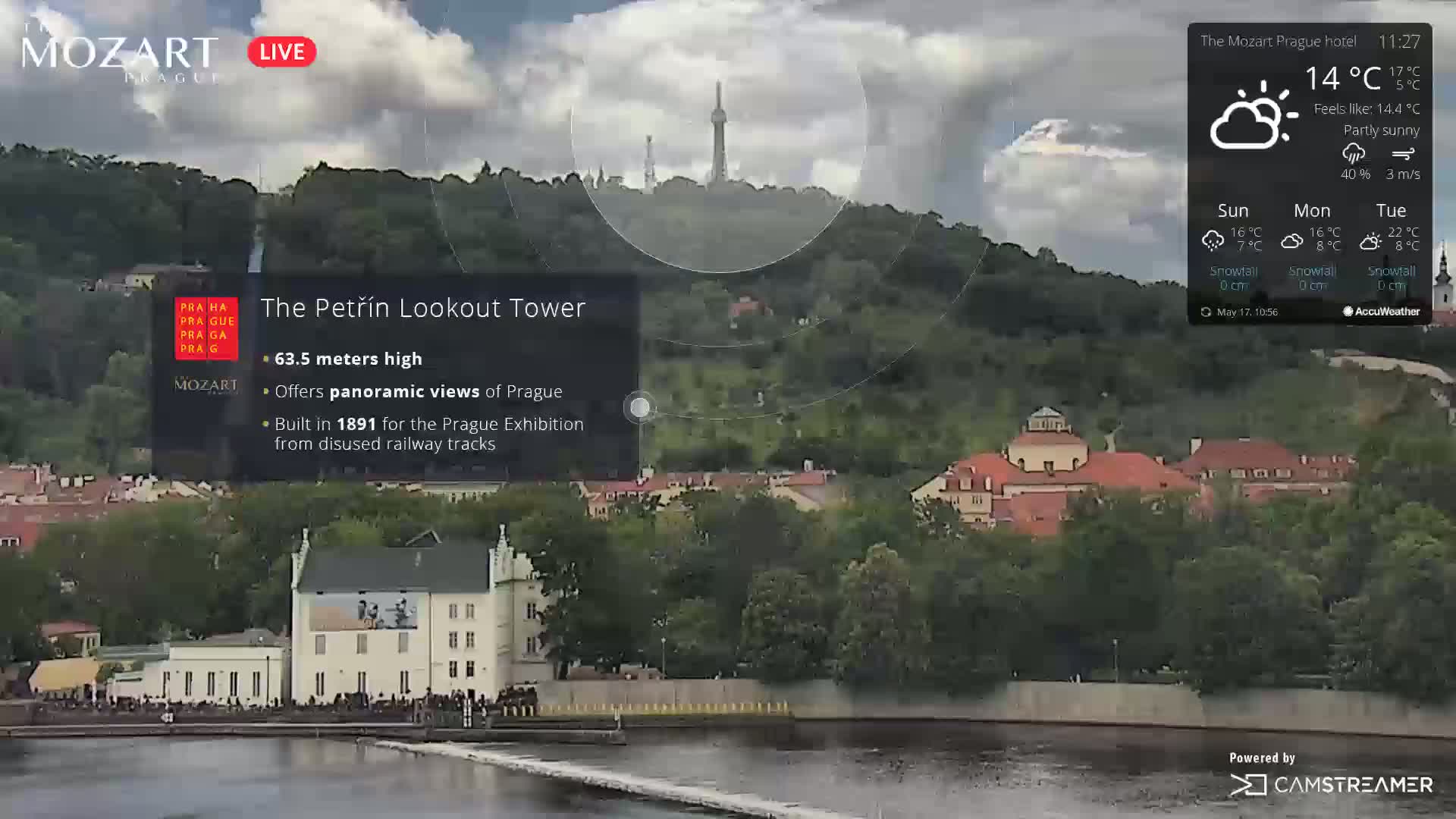 A partly sunny view of Prague, showcasing a tower overlooking a river and cityscape.