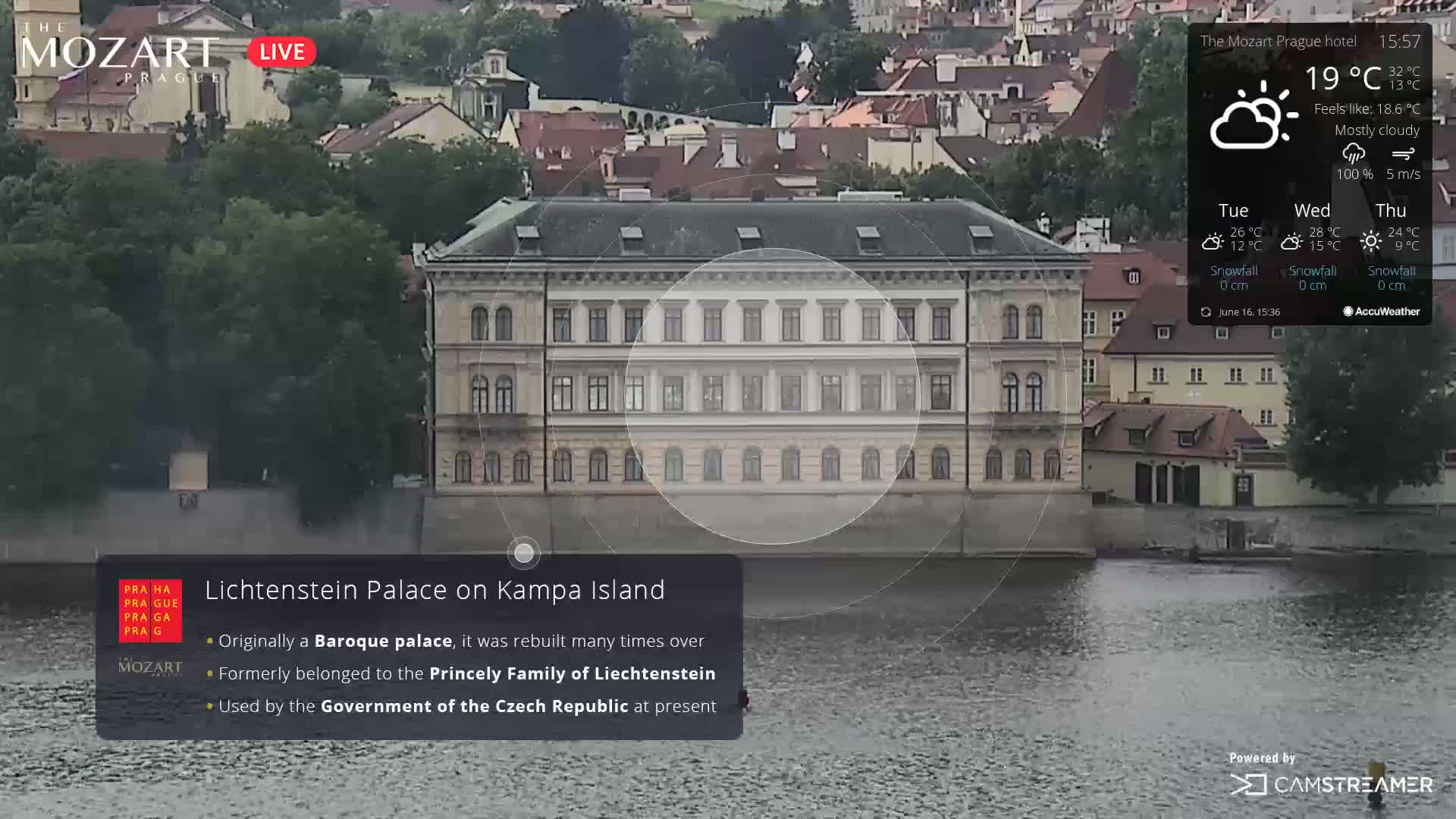 A Baroque palace sits on the bank of a river under mostly cloudy skies.