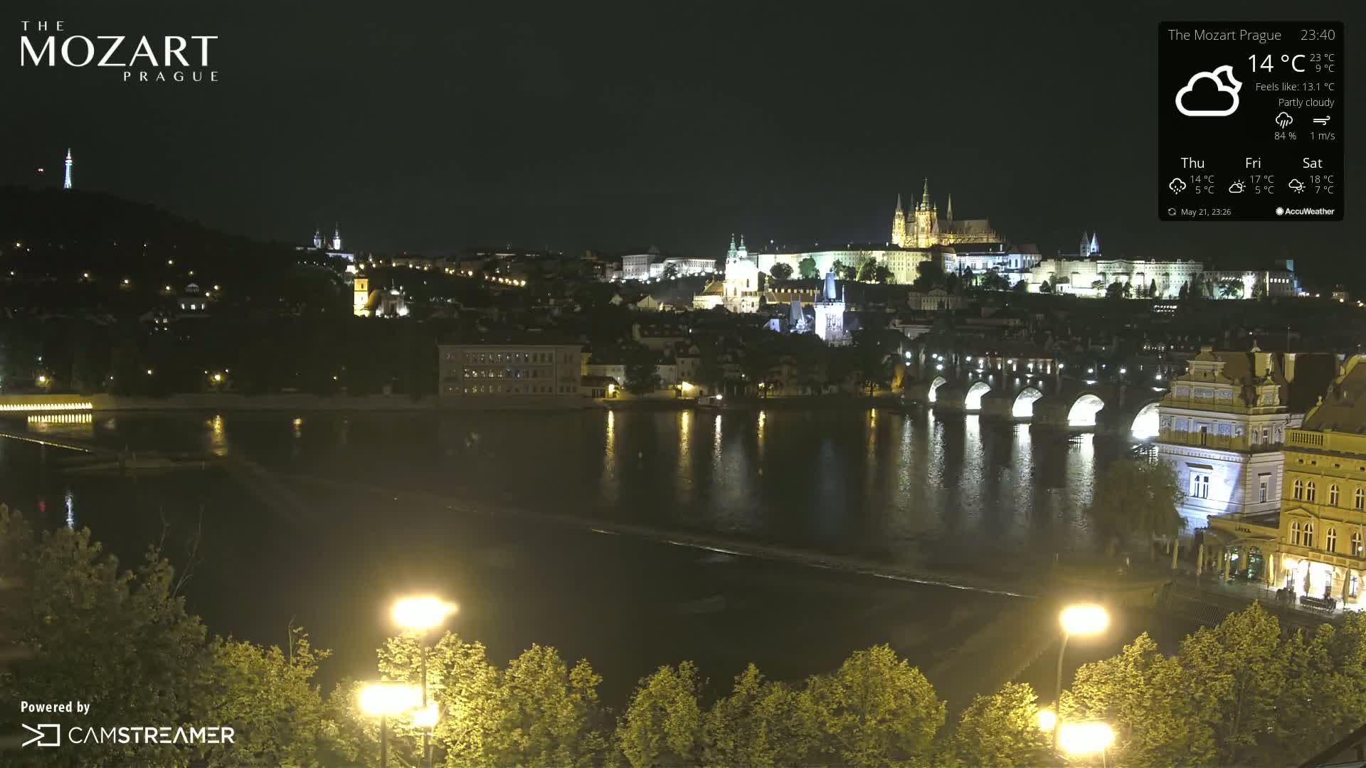 A nighttime view of a city with a river, bridges, and illuminated buildings under partly cloudy skies.