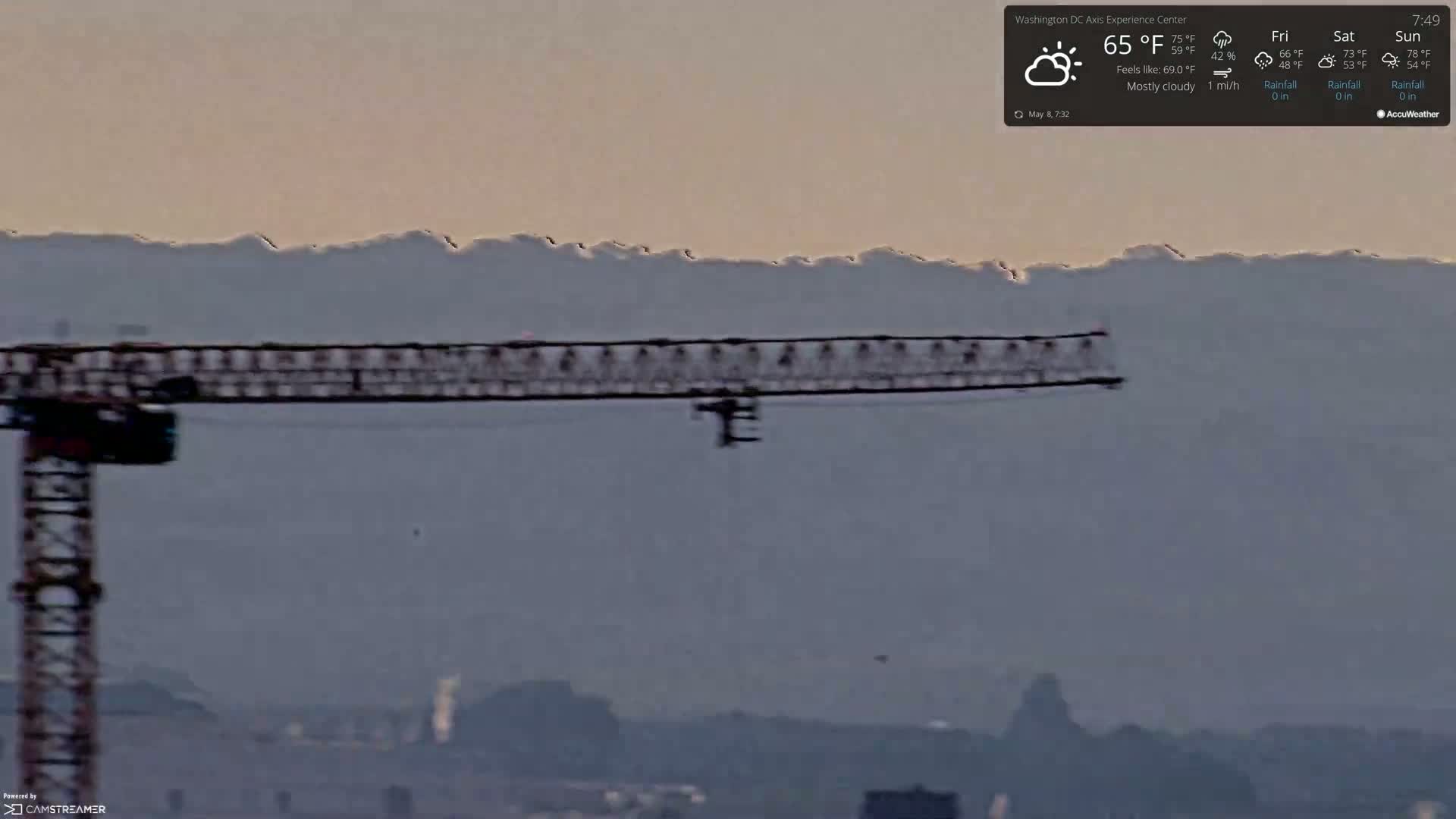 A construction crane is visible in the foreground against a mostly cloudy sky and distant hazy mountains.