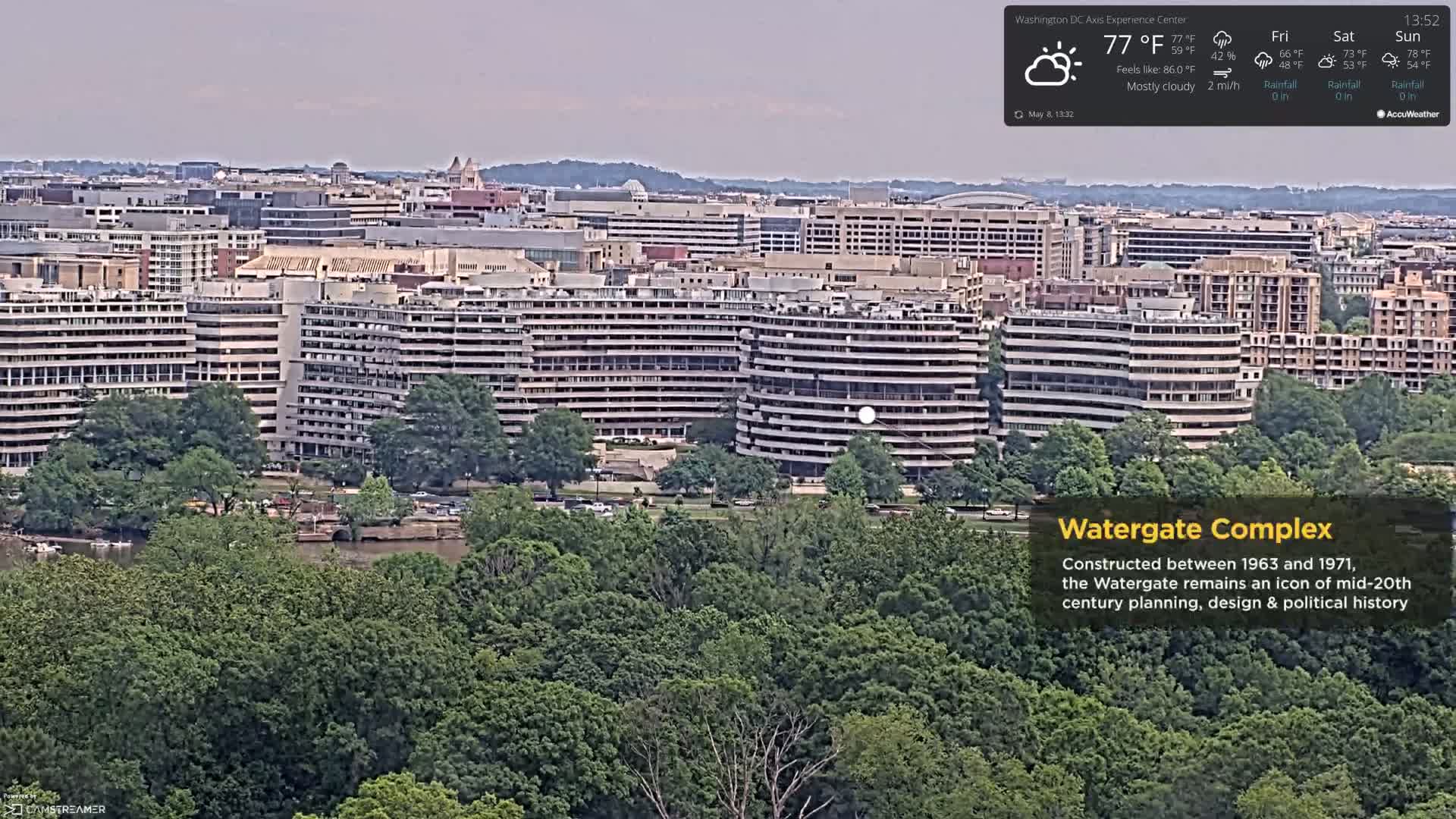 A mostly cloudy, breezy day overlooks the Watergate Complex, a large apartment complex situated near a river and surrounded by lush green trees.
