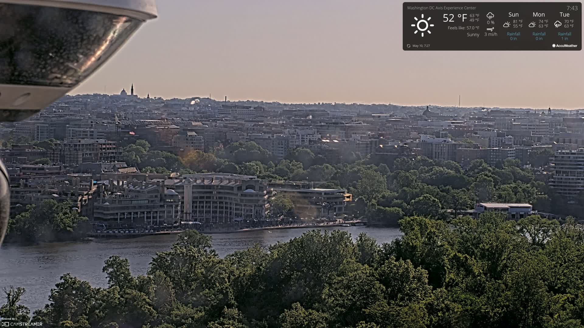 A sunny, hazy view of a city skyline and river, with lush green trees in the foreground.