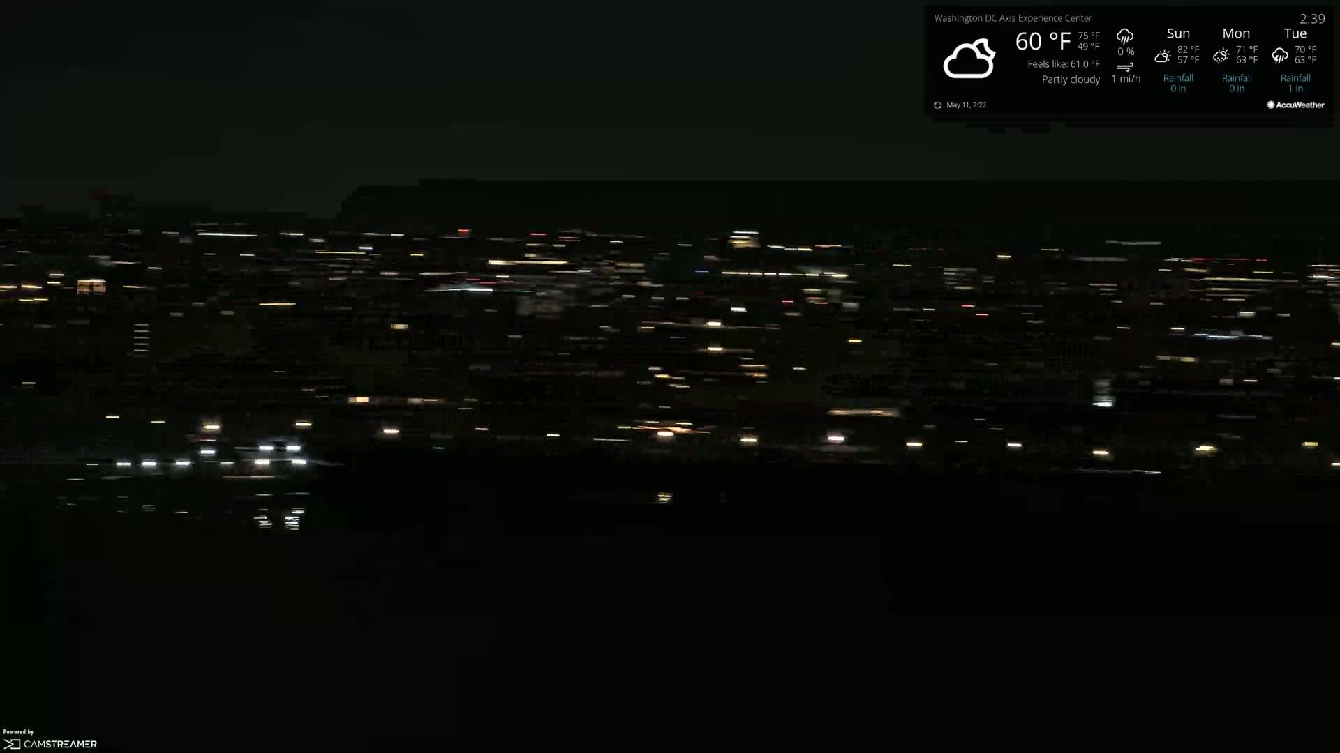 A nighttime long-distance view of a city with many blurry lights under partly cloudy skies.