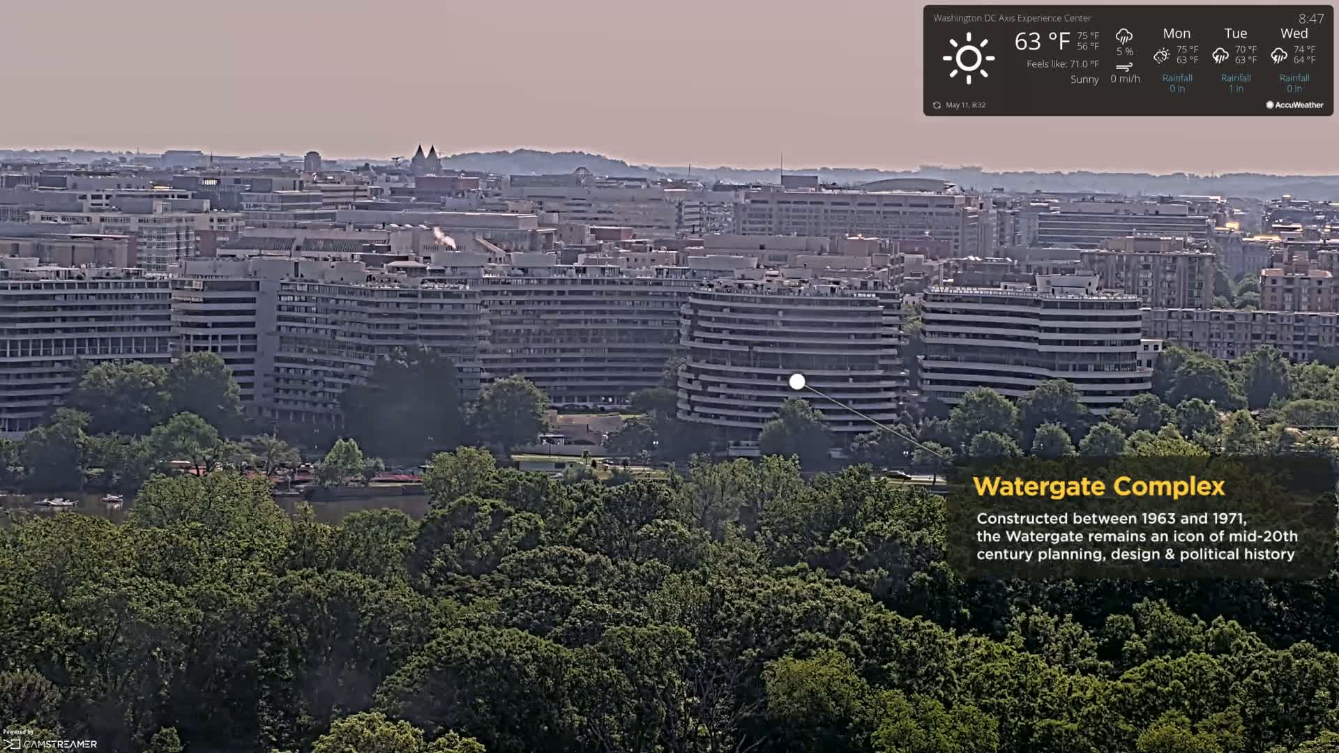 A sunny view of the Watergate Complex in Washington, D.C.,  surrounded by lush green trees and overlooking a cityscape.