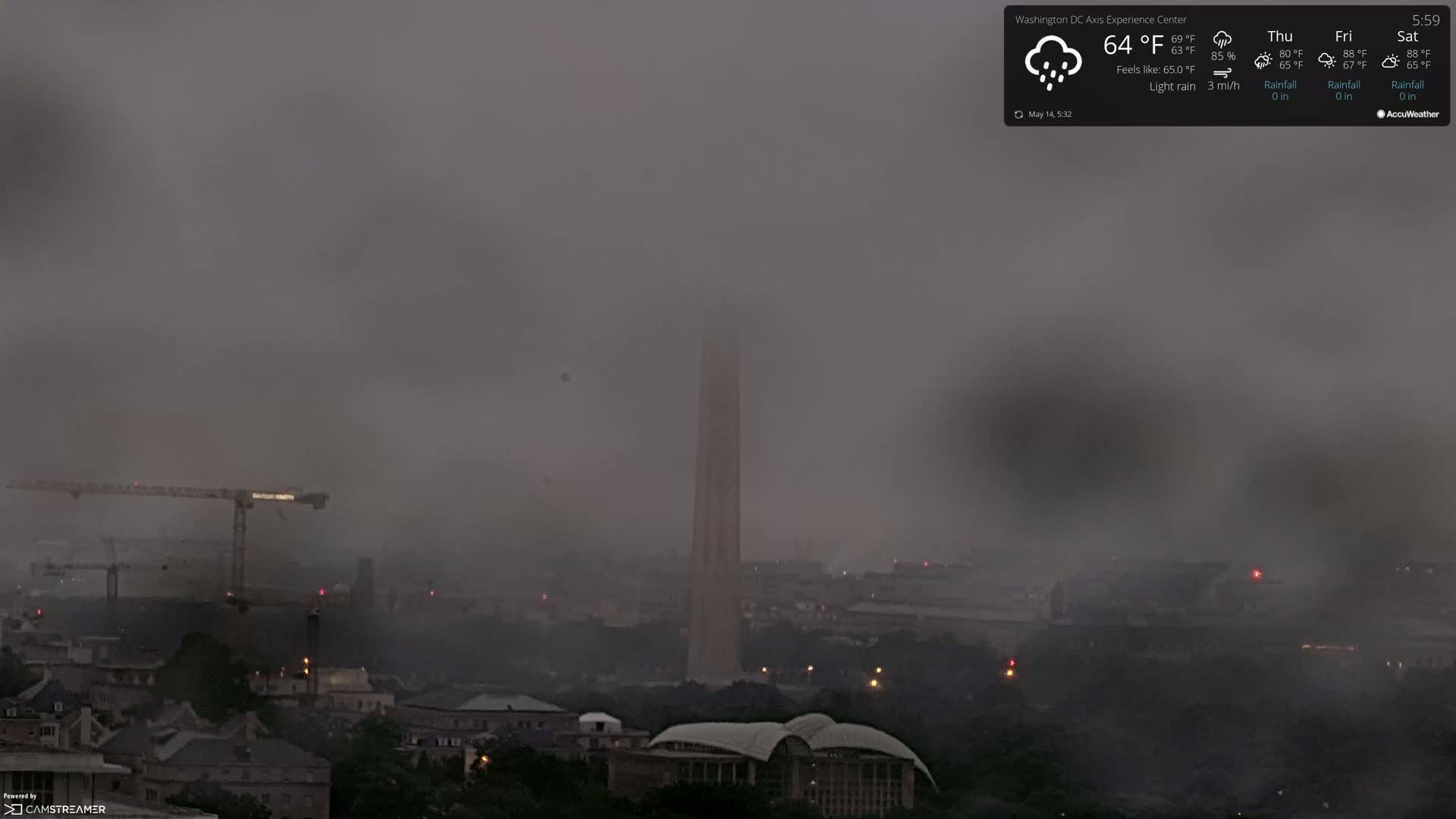 A hazy, light rain obscures a cityscape, with a tall monument visible in the center and construction cranes in the foreground.