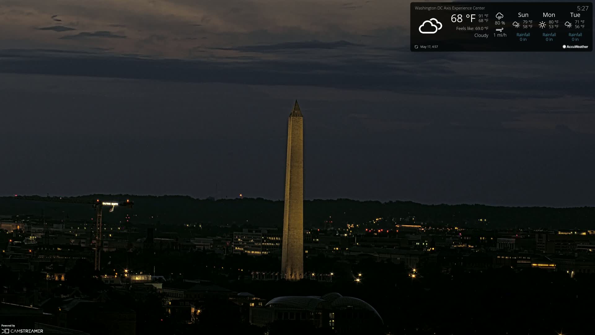 A dimly lit city at night, under cloudy skies, with the Washington Monument illuminated in the center.