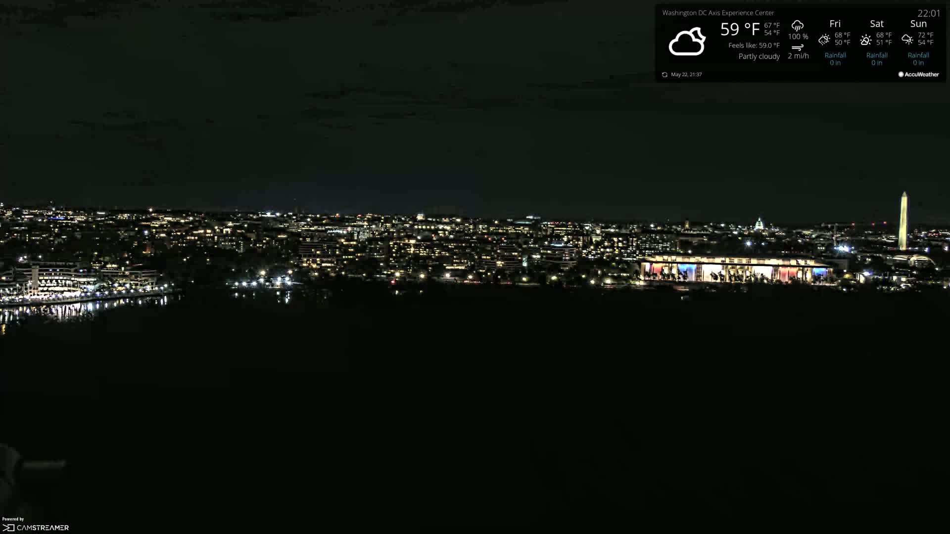 A nighttime view of a city skyline illuminated by lights, under partly cloudy skies.