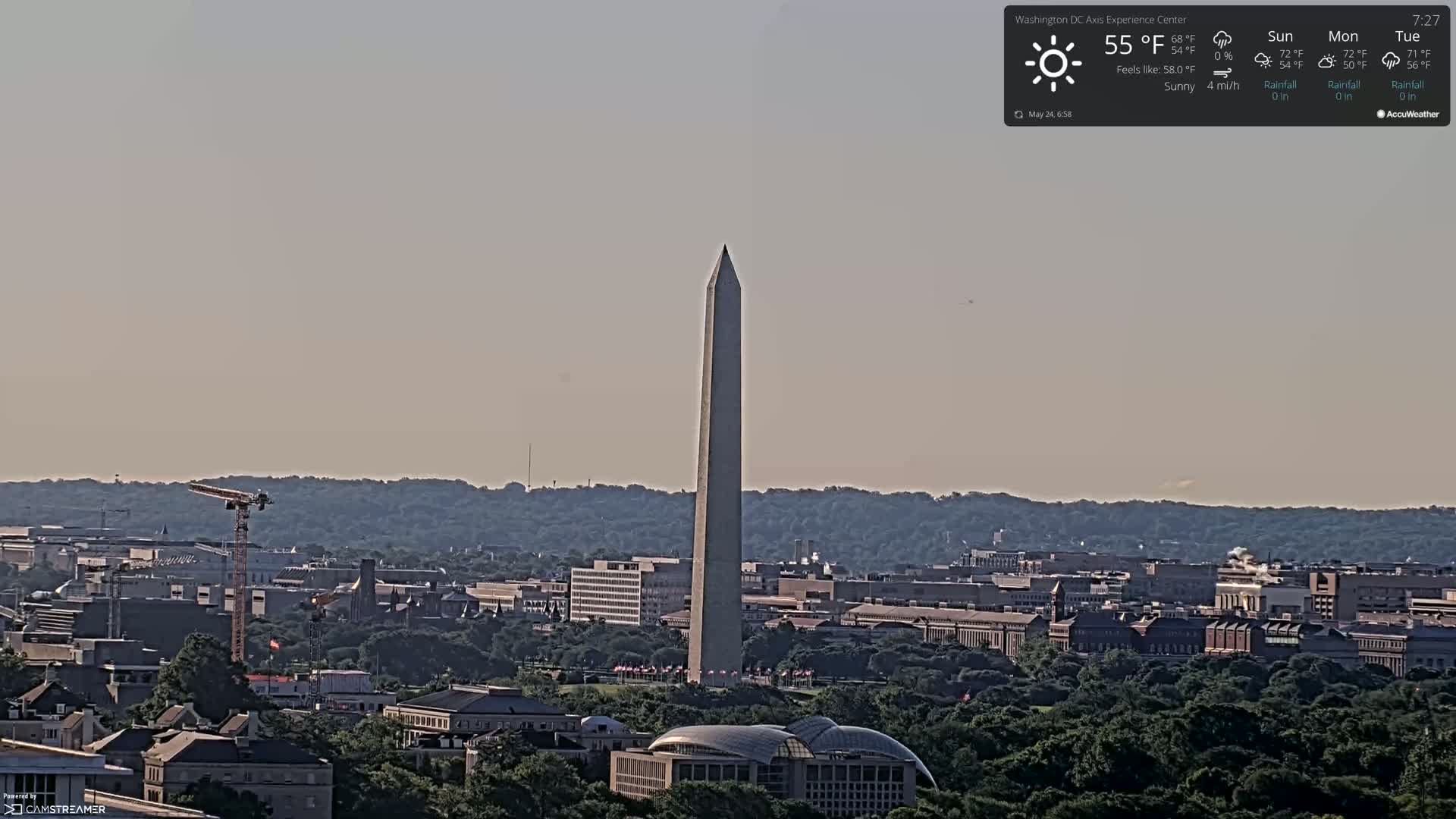 The Washington Monument stands tall amidst a sprawling cityscape under sunny skies, a light breeze blowing.