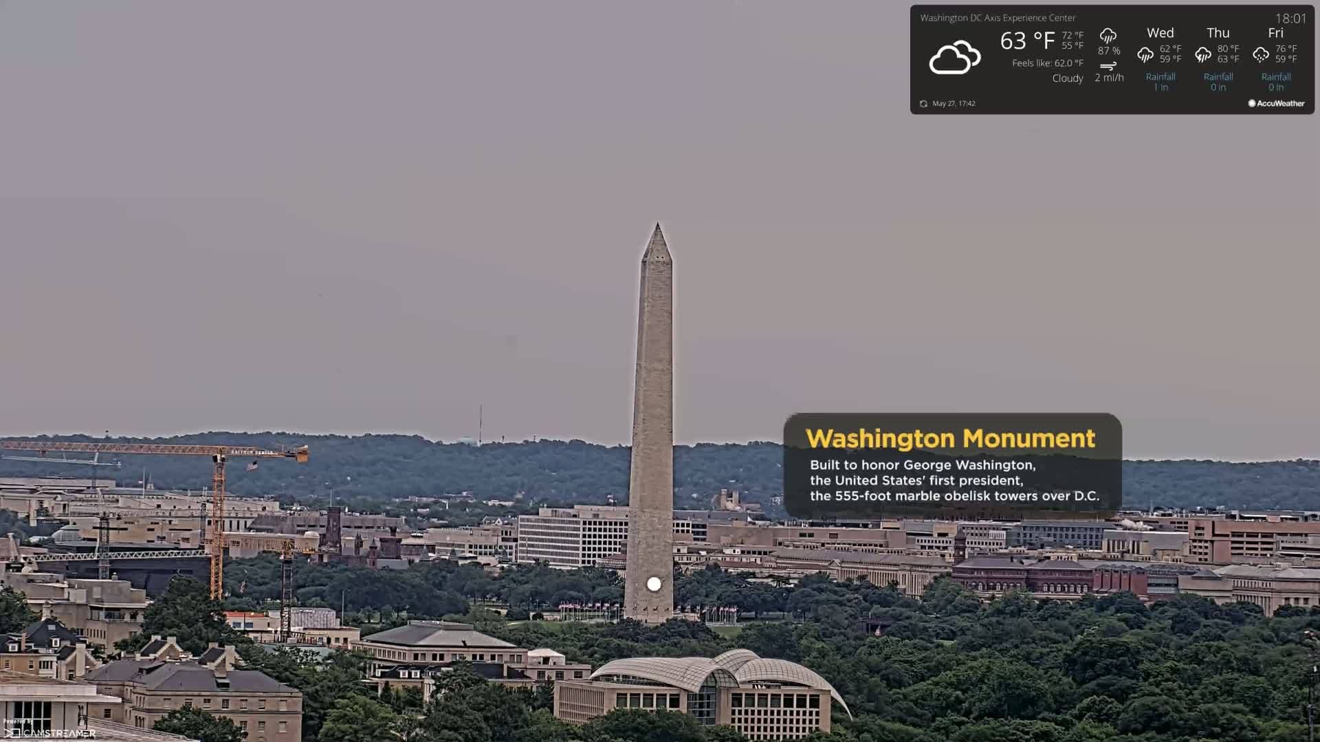 A tall, slender obelisk stands in the center of a sprawling city under a cloudy sky.