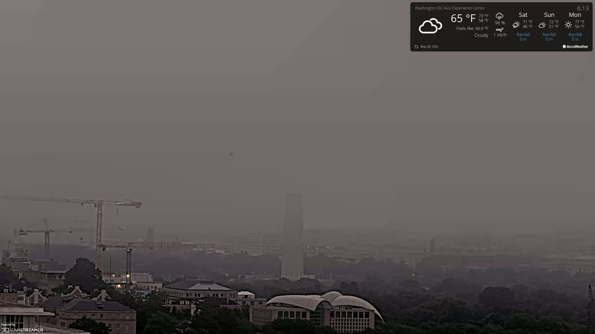 A hazy, cloudy cityscape is visible, with several construction cranes and buildings partially obscured by the atmospheric conditions.