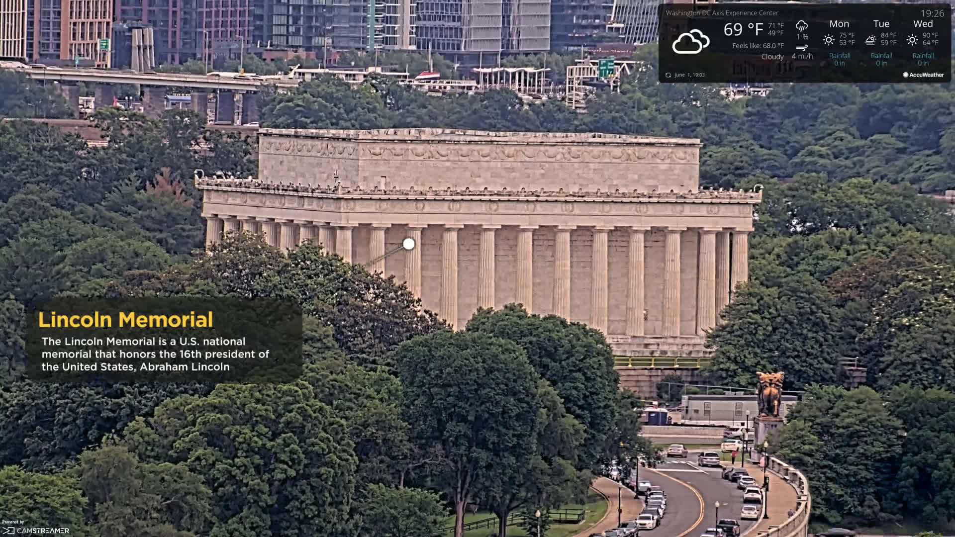 An elevated view of the Lincoln Memorial on a cloudy day, surrounded by lush green trees and a road with cars.