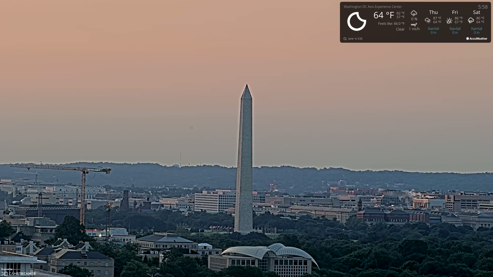An expansive view of Washington, D.C., under a clear, pale pink twilight sky, features the Washington Monument prominently in the foreground, with a cityscape and distant hills in the background.