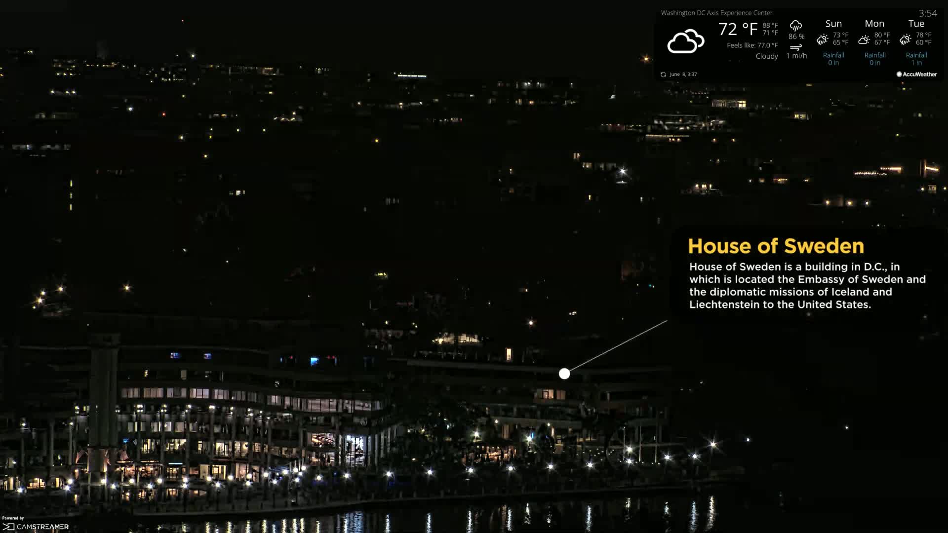 A nighttime, cloudy view of a waterfront building complex with lights illuminating the area.