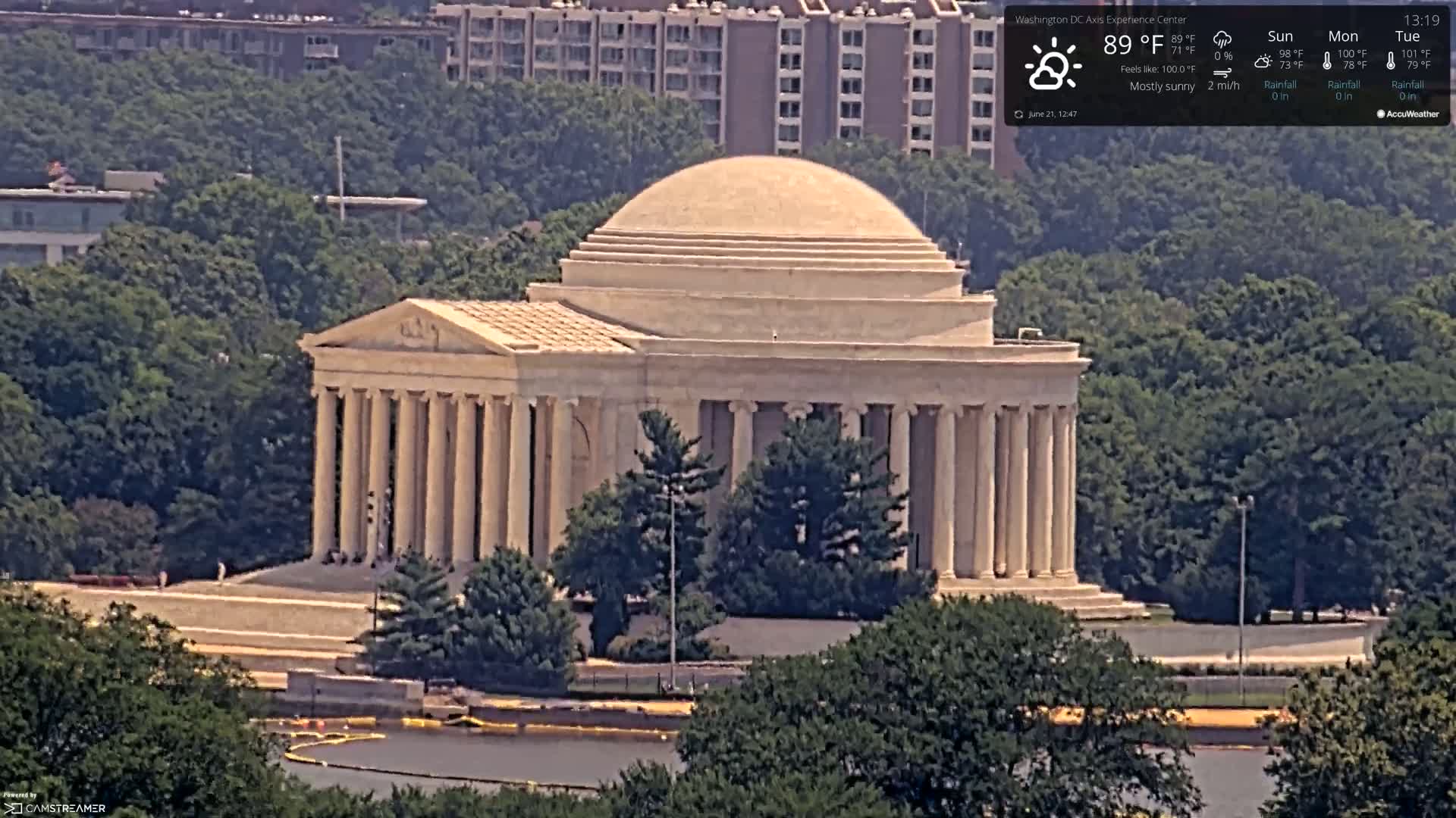 A large, classical-style building with a dome sits amidst green trees on a mostly sunny day.