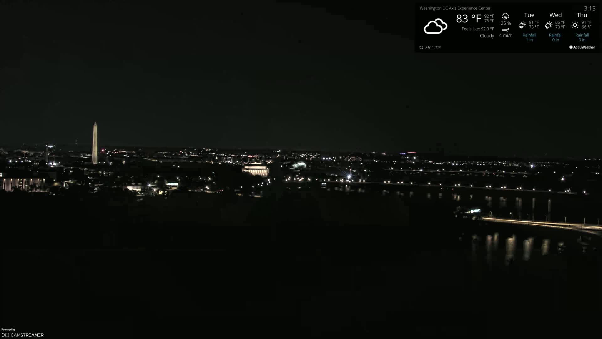 A nighttime, cloudy view of a city skyline, featuring a tall monument, with dimly lit roads and bodies of water visible.