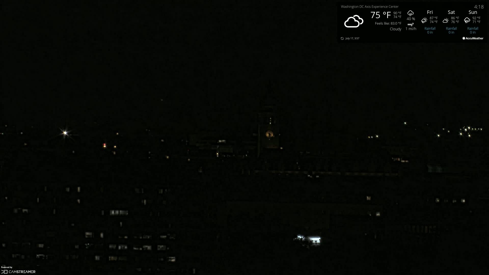 A nighttime, cloudy view of a city skyline with sparsely lit buildings and a prominent clock tower in the distance.