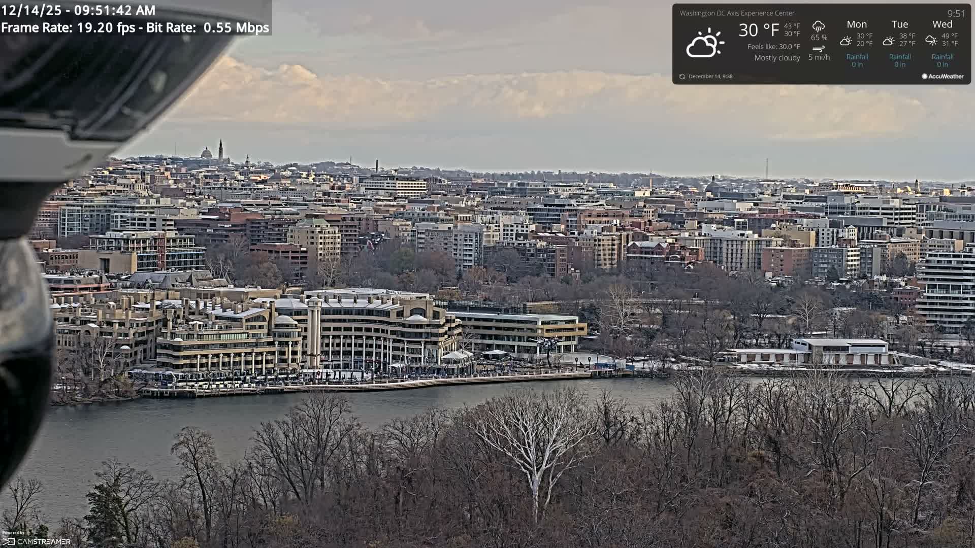 A clear night cityscape features numerous illuminated buildings, a prominent obelisk, and a bridge with streaking vehicle lights reflecting on the dark water below.