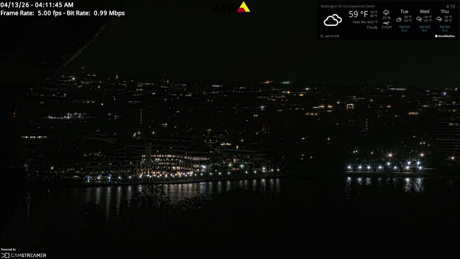 A clear night cityscape features numerous illuminated buildings, a prominent obelisk, and a bridge with streaking vehicle lights reflecting on the dark water below.