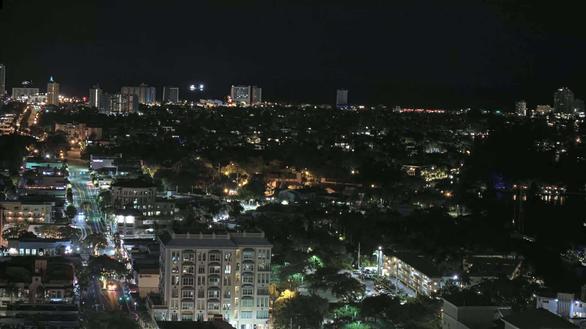 A nighttime aerial view shows a city with numerous buildings and streets illuminated, under a clear, dark sky.