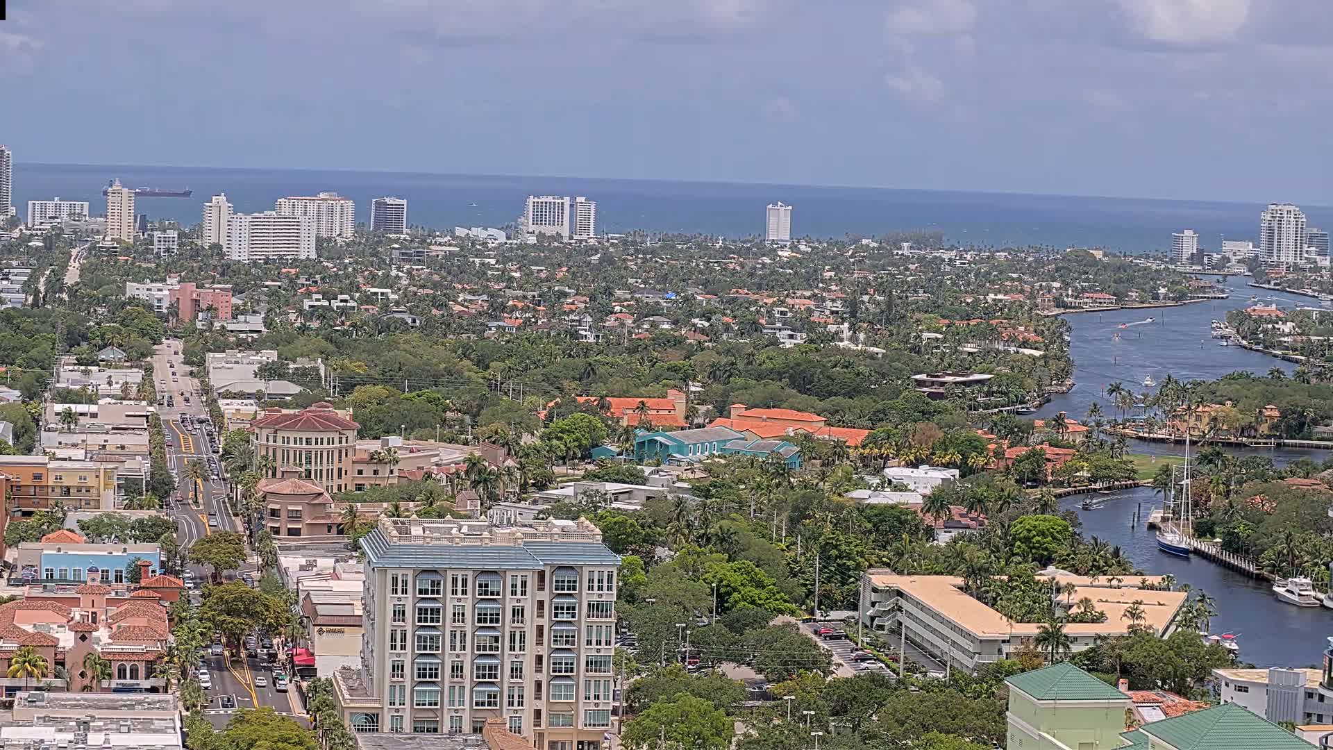 A coastal city with a waterway meandering through a dense, lush landscape of residential buildings under a partly cloudy sky.