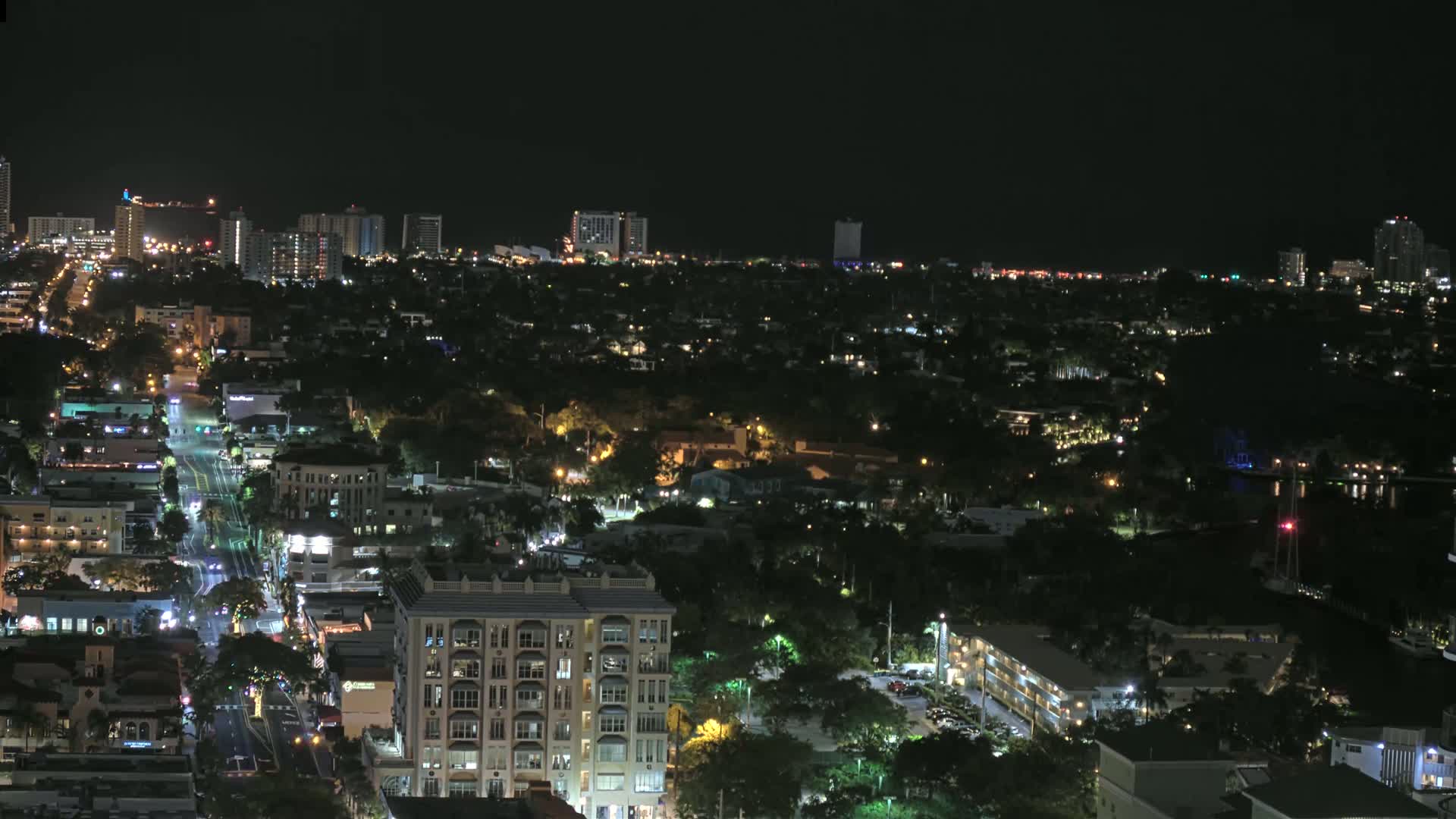 A nighttime aerial view of a city with a mix of residential buildings and businesses, illuminated by streetlights and building lights.
