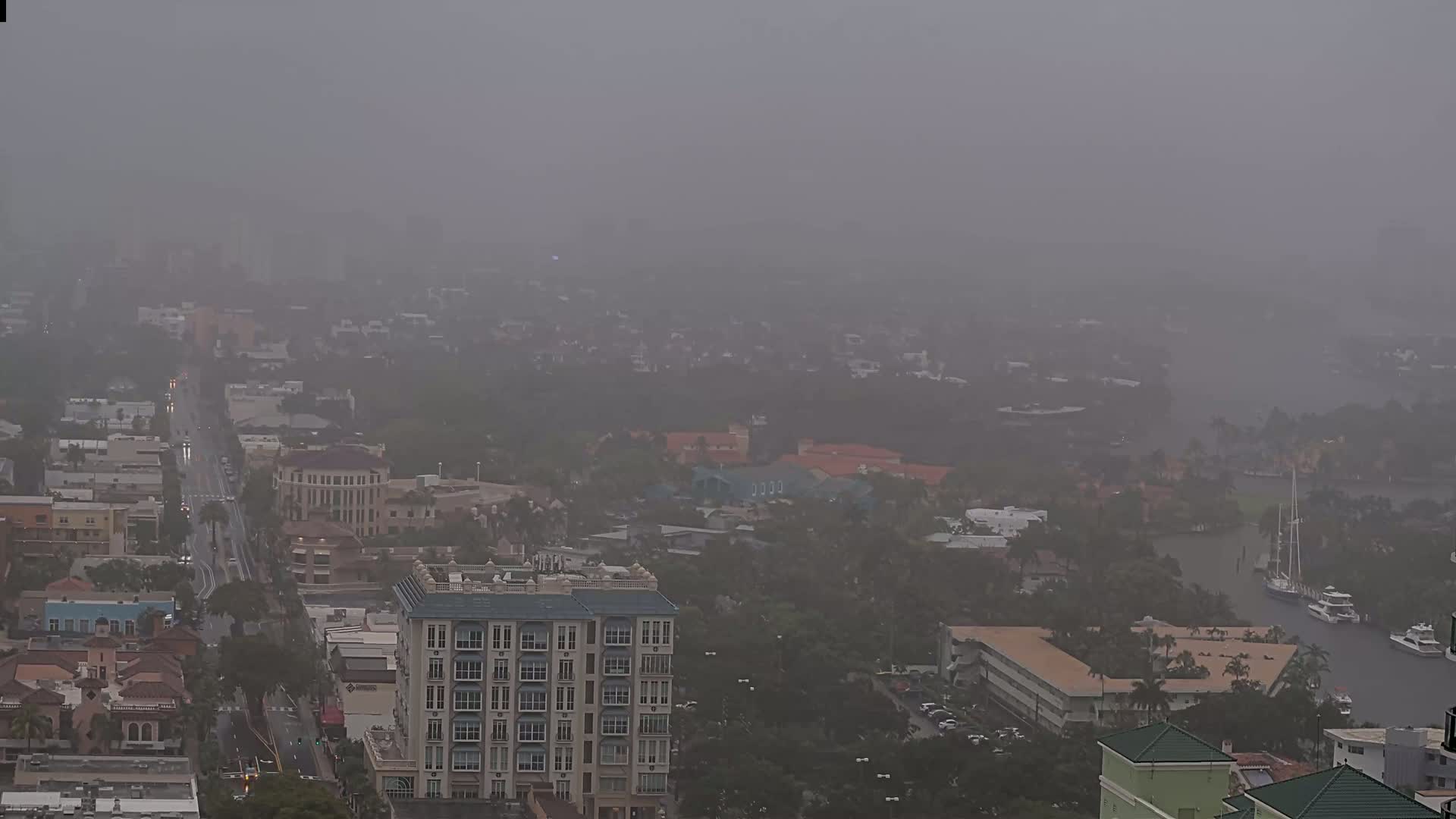 A hazy, overcast day reveals a city scene with buildings, roads, and waterways, partially obscured by atmospheric dust or mist.