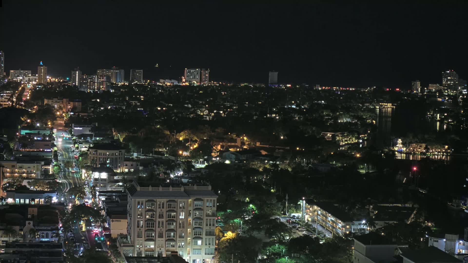 A nighttime aerial view of a city illuminated by streetlights and building lights, with a dark body of water visible in the distance.