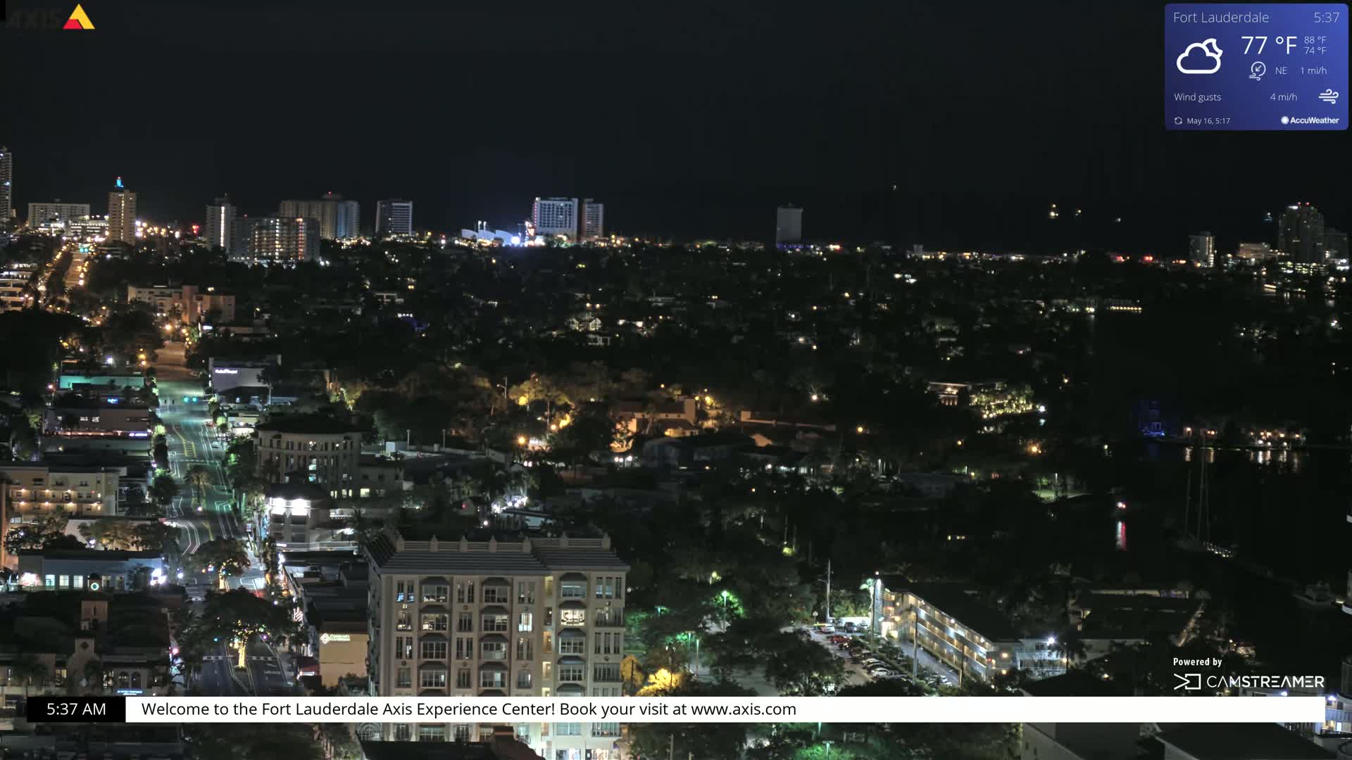 A nighttime, high-angle view of a city illuminated by streetlights and building lights under partly cloudy skies.