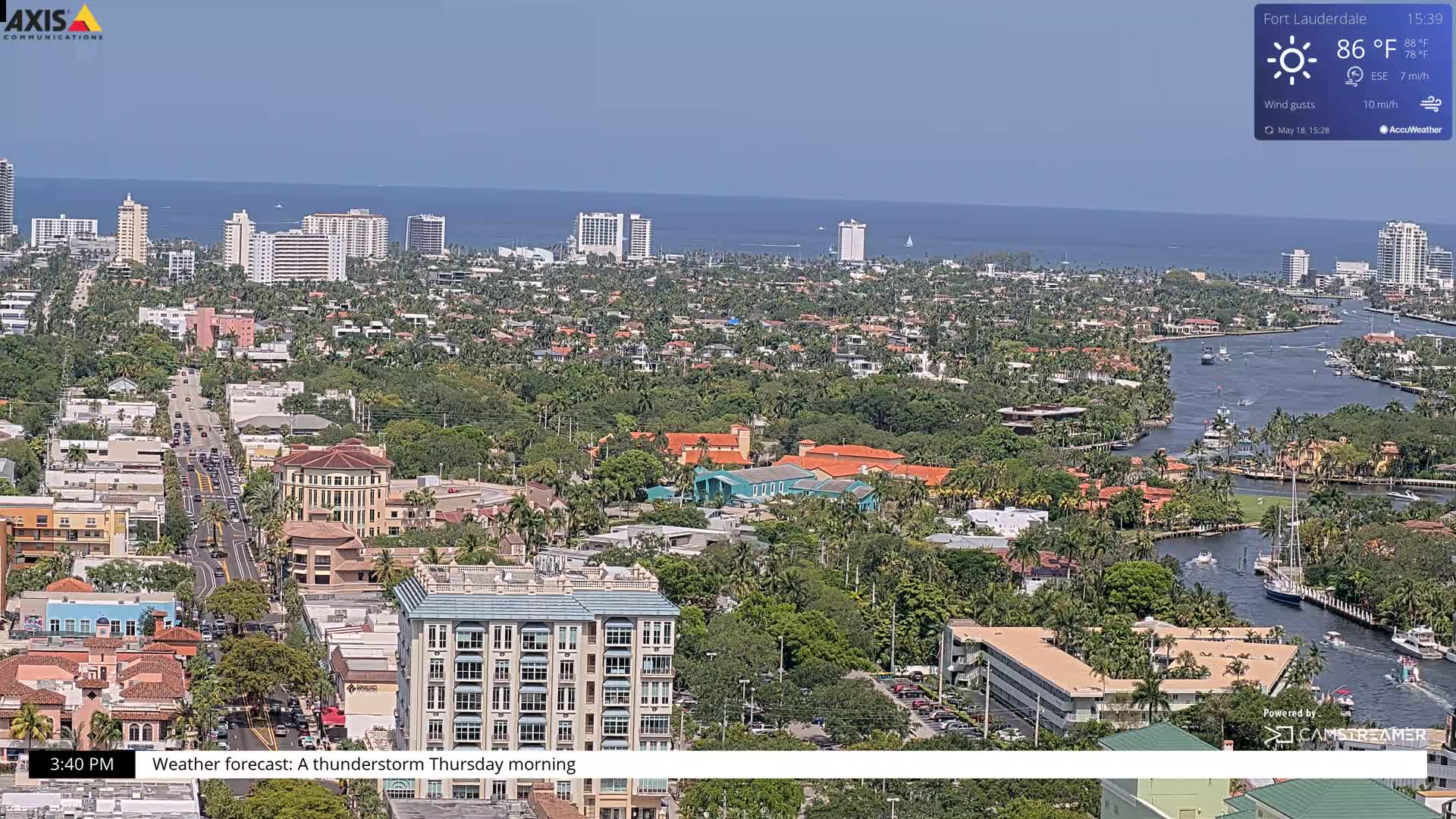 A high-angle, long shot of a coastal city on a partly sunny day, showing a waterway winding through residential areas towards the ocean.
