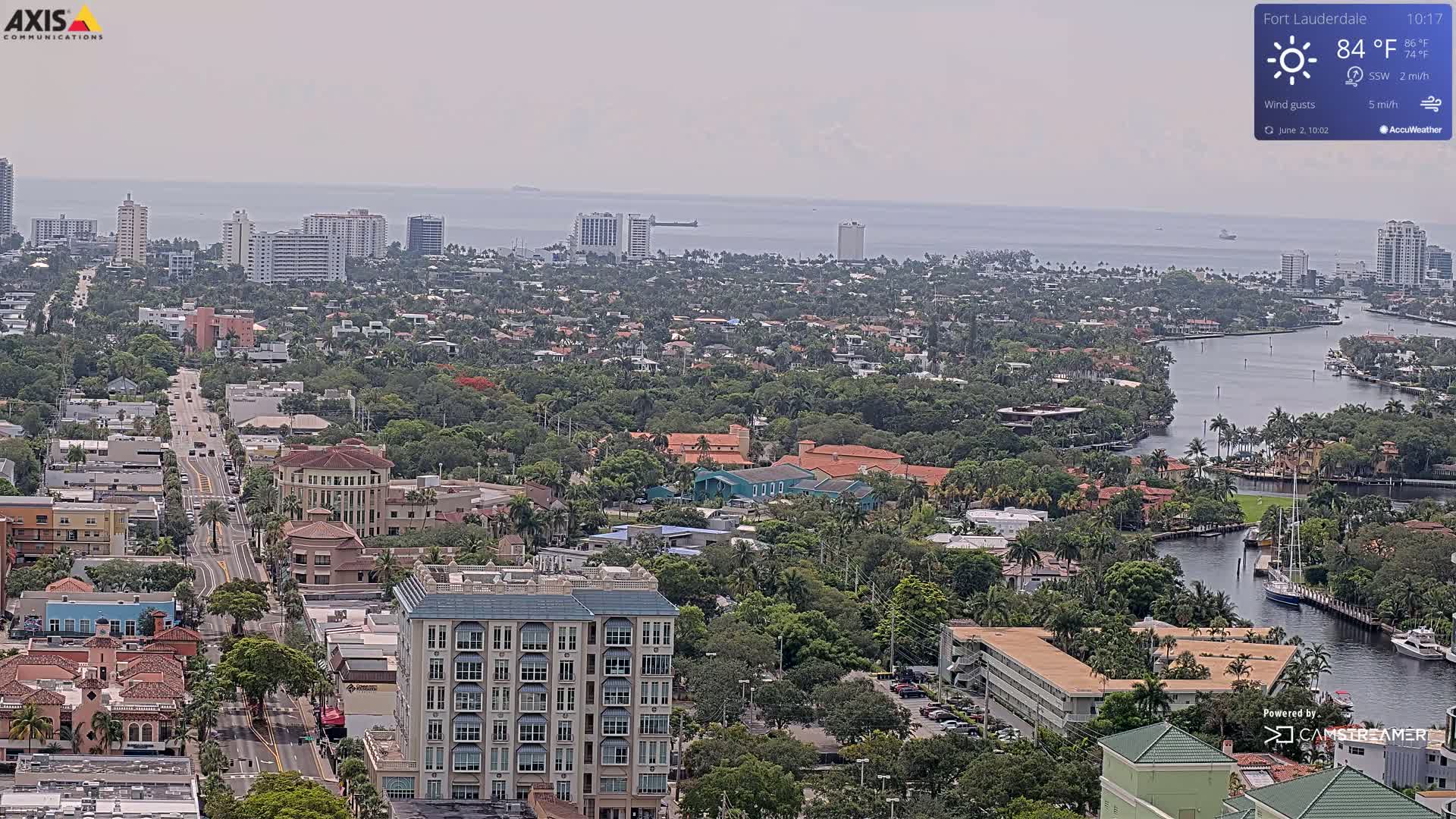 An aerial view of a city on a hazy day shows a waterfront area with a waterway cutting through residential neighborhoods,  high-rise buildings near the water, and many low-rise buildings further inland.