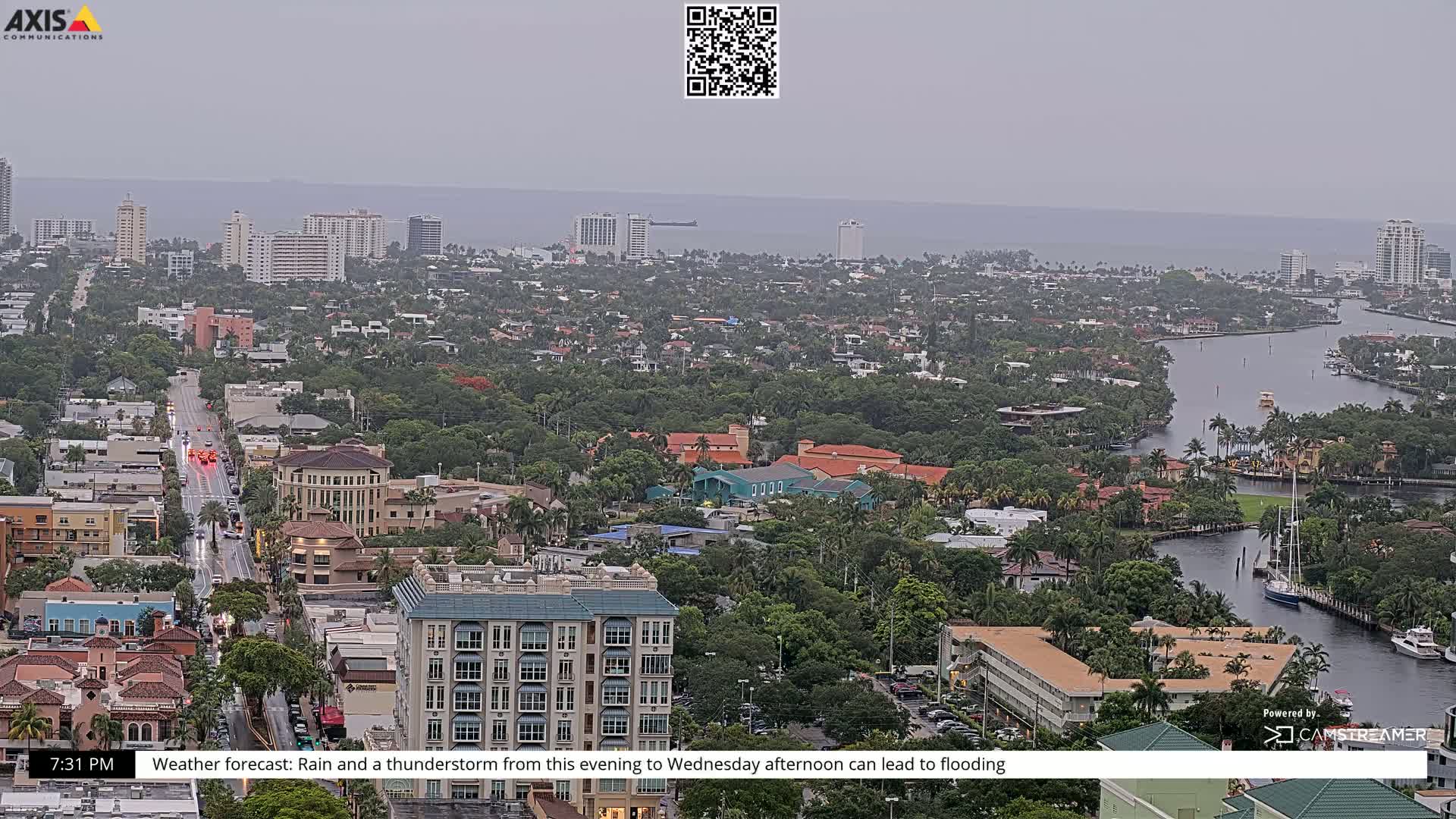 A coastal city with numerous buildings and waterways is seen under overcast skies with rain.