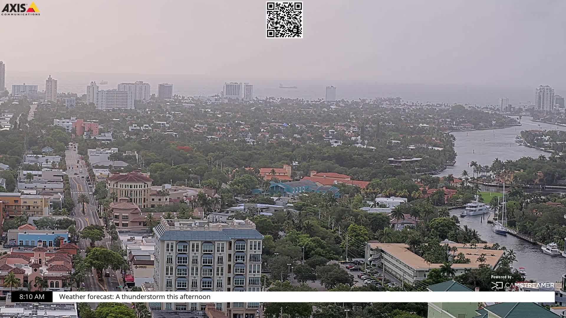 A hazy, aerial view shows a coastal city with a waterway winding through residential areas and high-rise buildings.