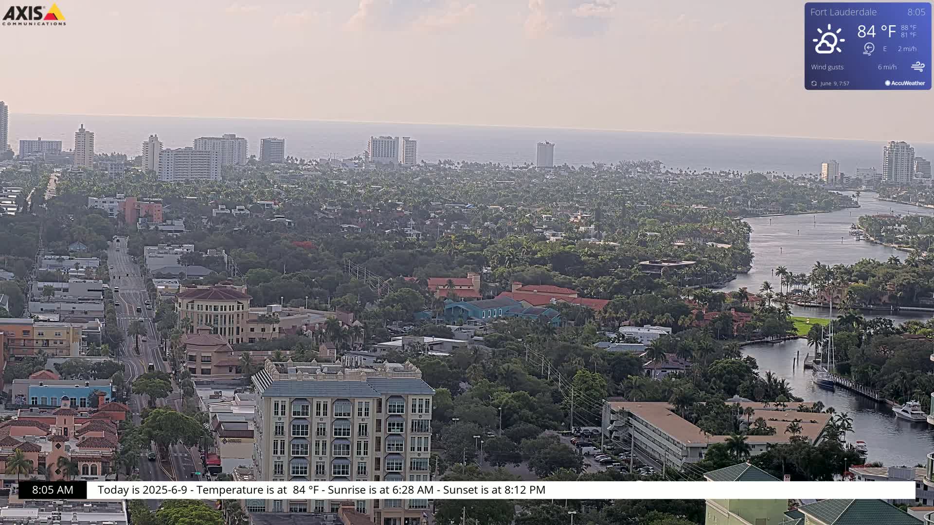 An aerial view of a coastal city on a hazy day, showing a waterway winding through a residential area towards the ocean.