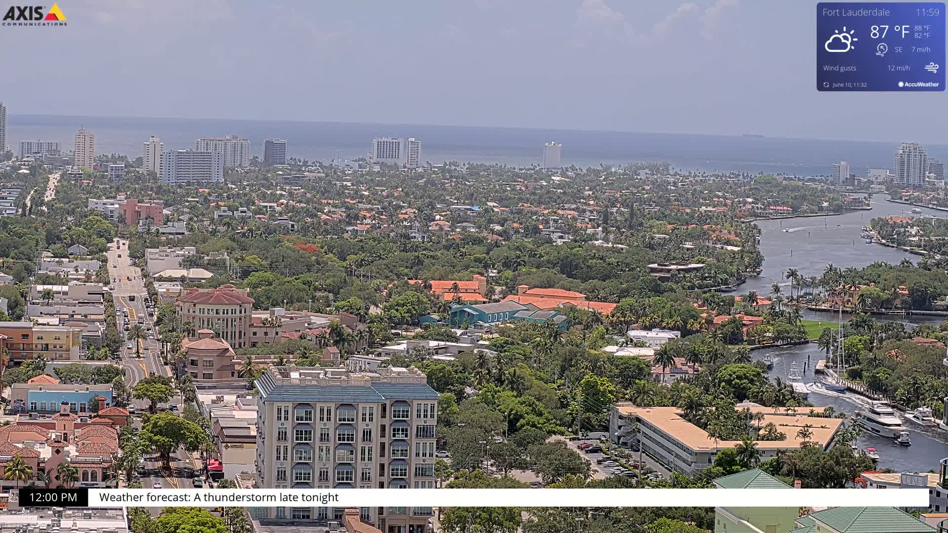 An aerial view shows a coastal city on a partly sunny day with a waterway winding through a neighborhood of houses and buildings near the ocean.