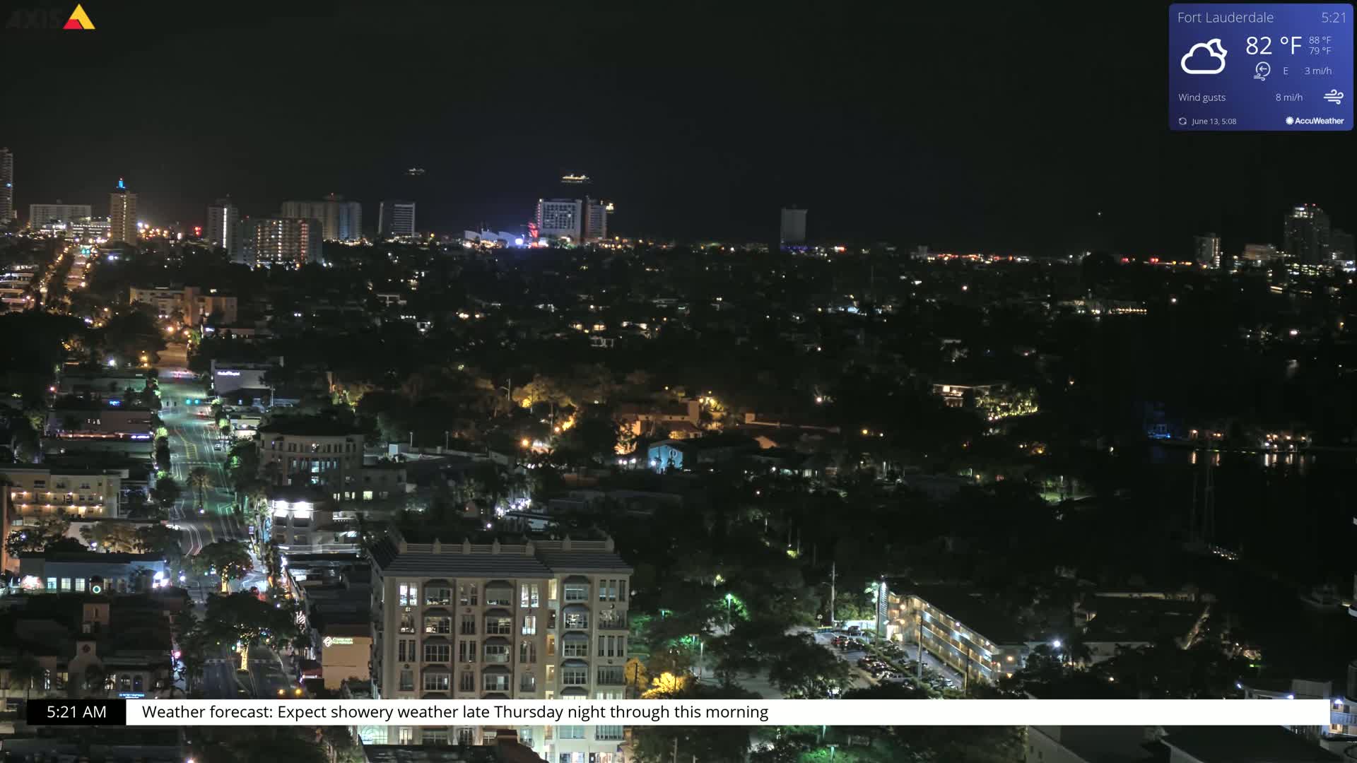 A nighttime aerial view of a city with many buildings illuminated, under partly cloudy skies.
