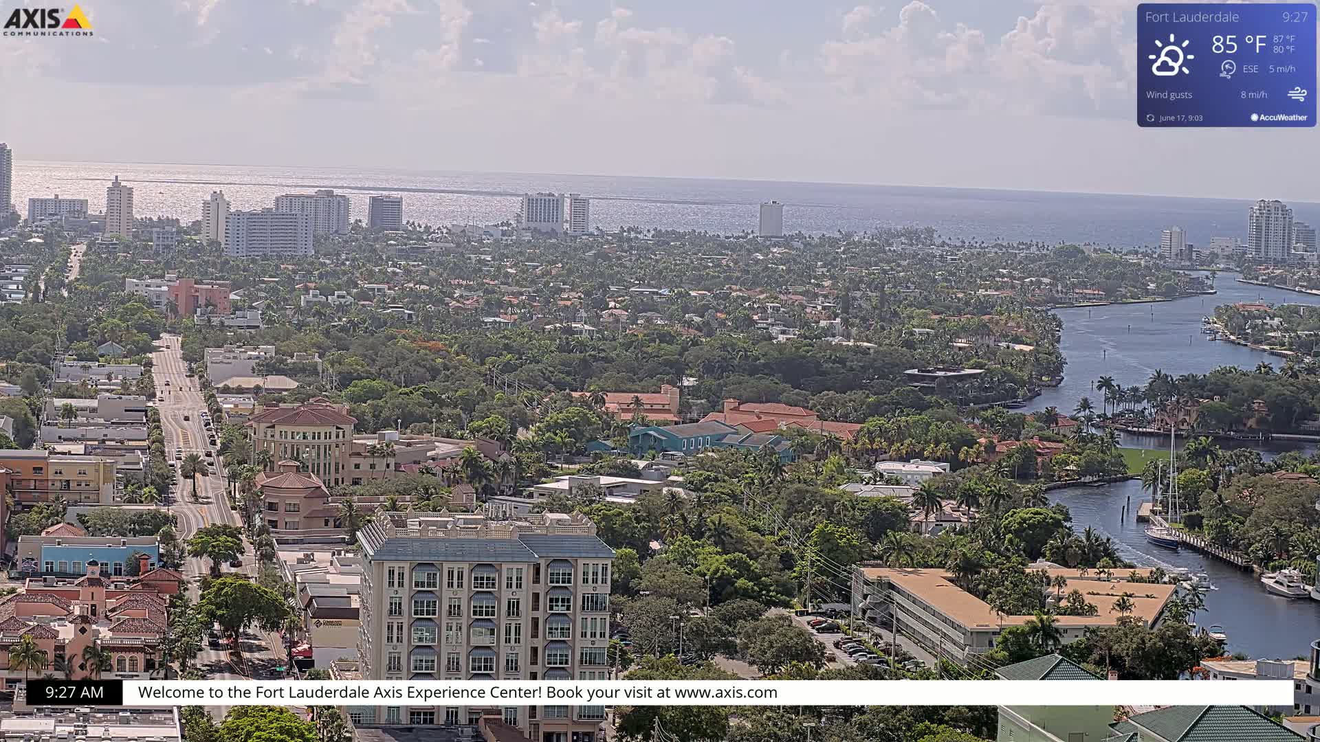 A sprawling coastal city with a waterway winds through a residential area under partly cloudy skies.