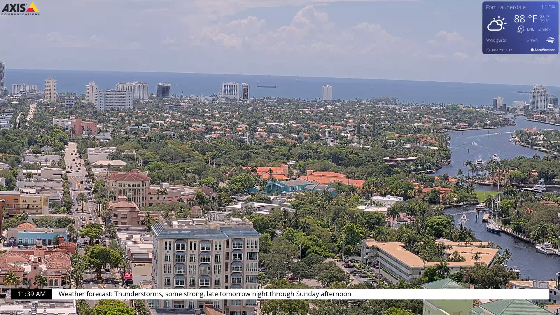 An aerial view shows a coastal city with waterways under partly cloudy skies, and a forecast of thunderstorms.