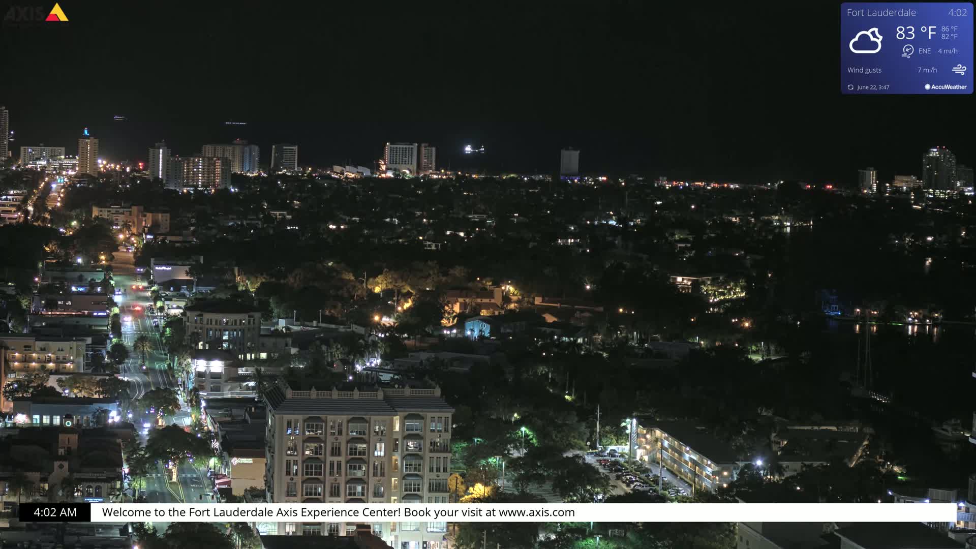 A nighttime aerial view of a city with numerous lit buildings and streets under partly cloudy skies.