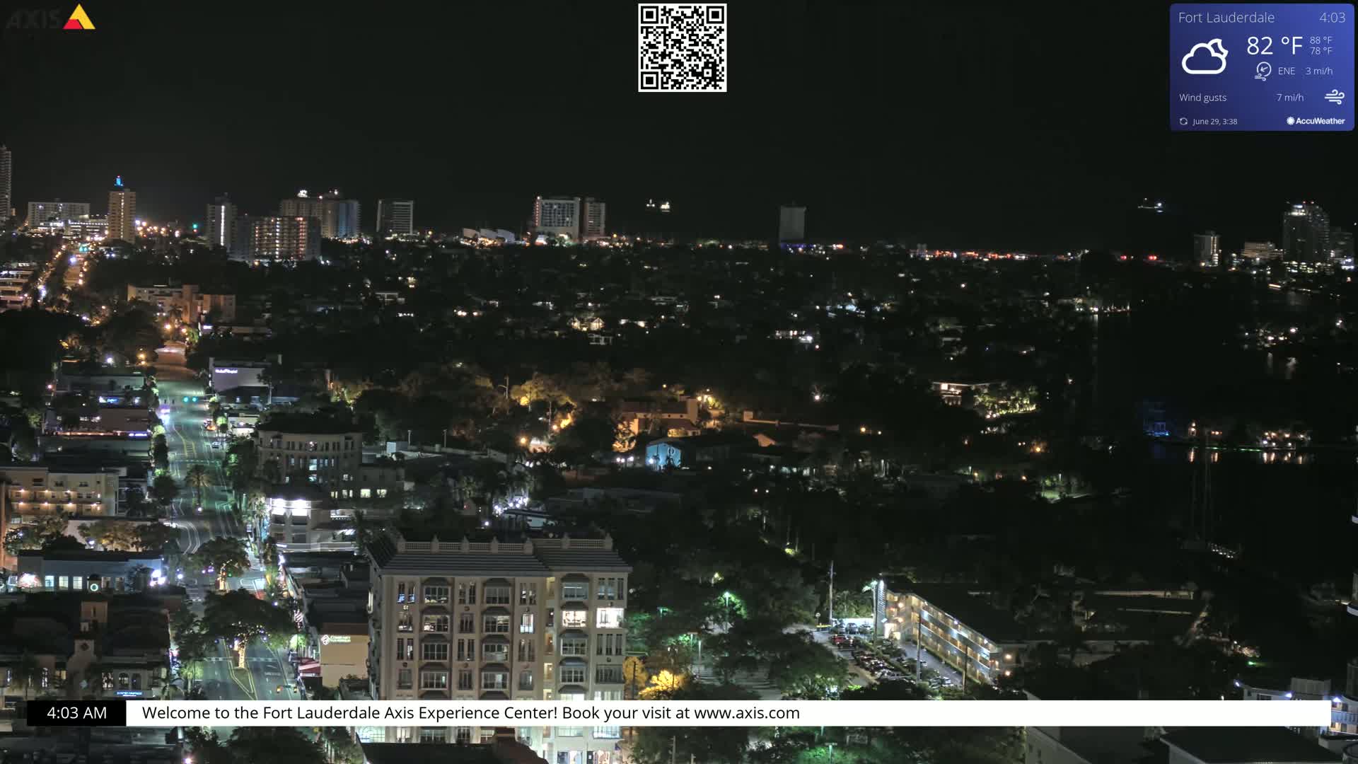 A nighttime aerial view of a city illuminated with streetlights and building lights under partly cloudy skies.
