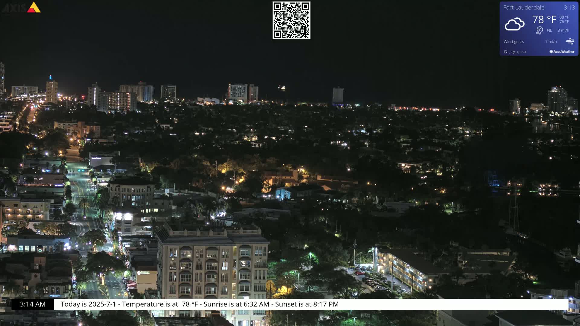 A nighttime, aerial view of a city with illuminated buildings and streets under partly cloudy skies.
