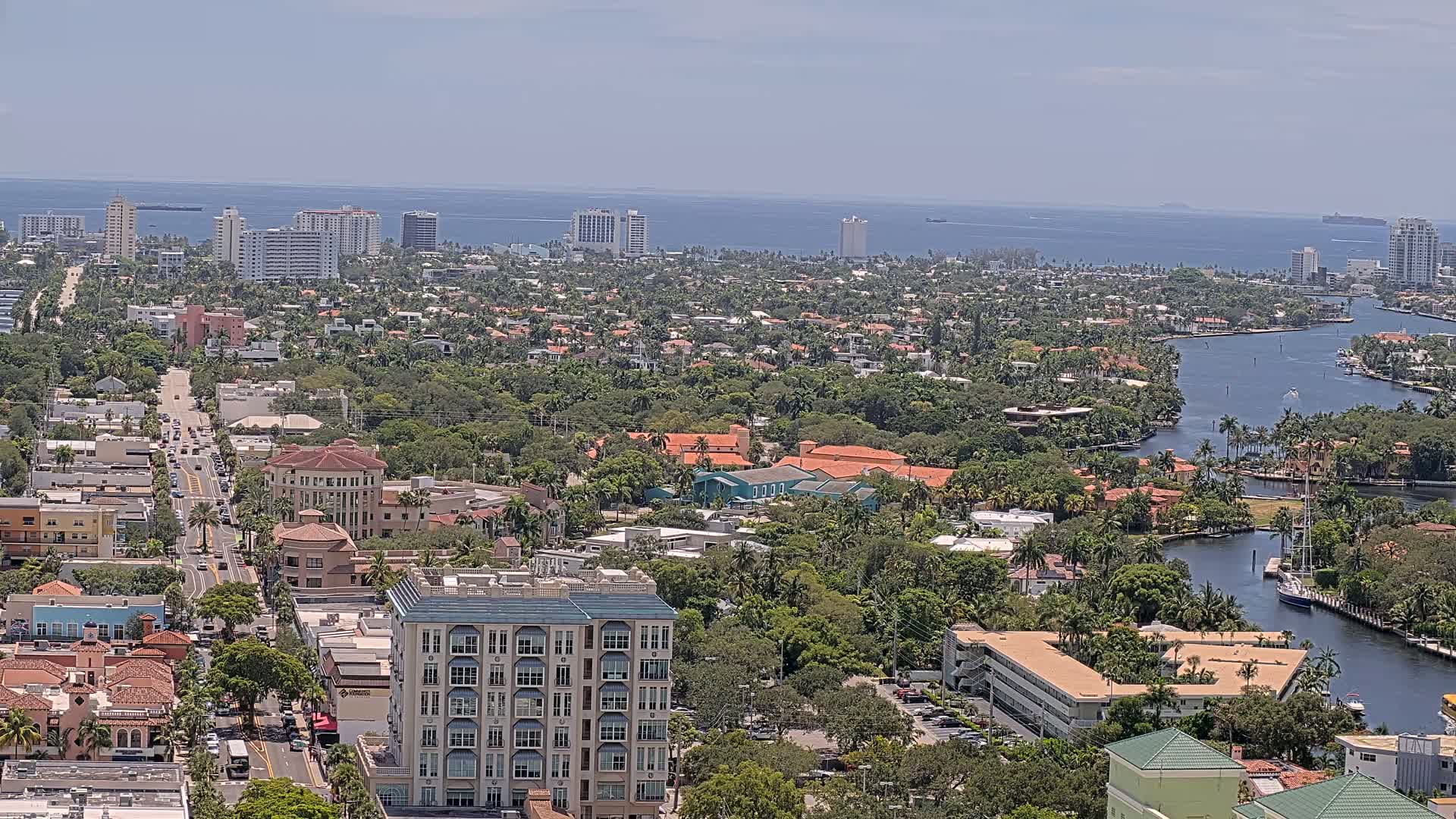 A coastal city with a waterway meandering through a dense, lush landscape of houses and high-rise buildings under a clear, sunny sky.