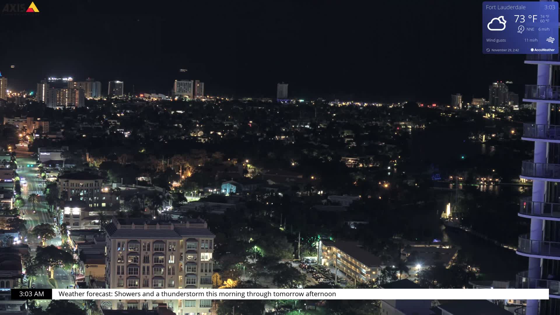 An elevated nighttime view showcases a sprawling city illuminated by countless building and street lights, with reflections shimmering on a body of water, all under a clear dark sky.