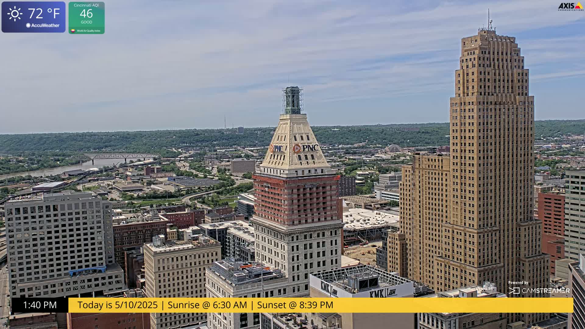 A high-angle, sunny view of a city skyline featuring two tall buildings, one under construction, with a river and bridges visible in the distance.