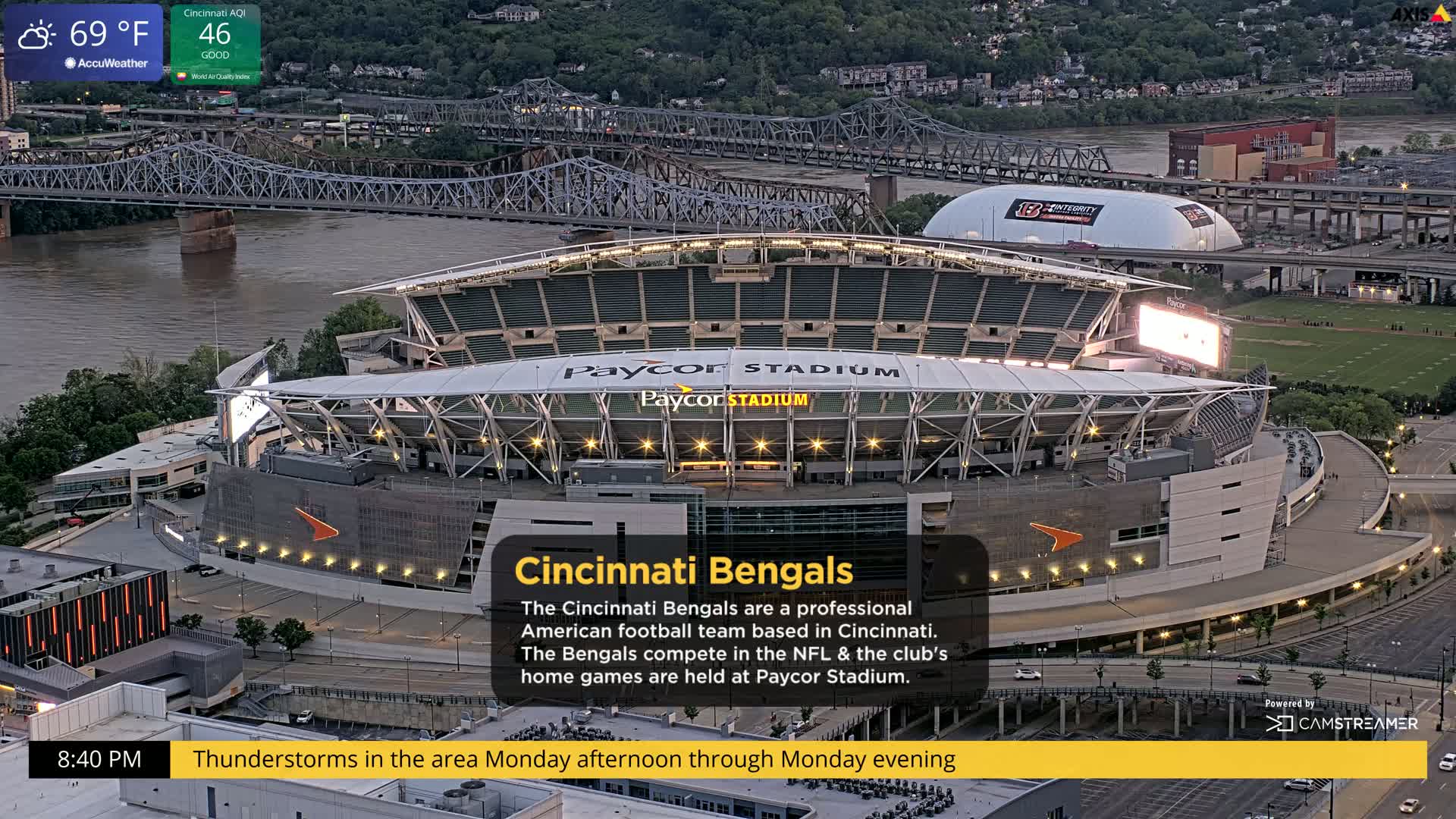 An aerial view of Paycor Stadium at dusk, with a river and bridges in the background, under a partly cloudy sky.