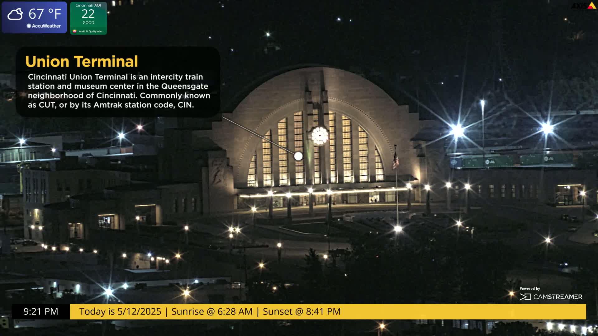 A large, illuminated train station stands at night under a partly cloudy sky.